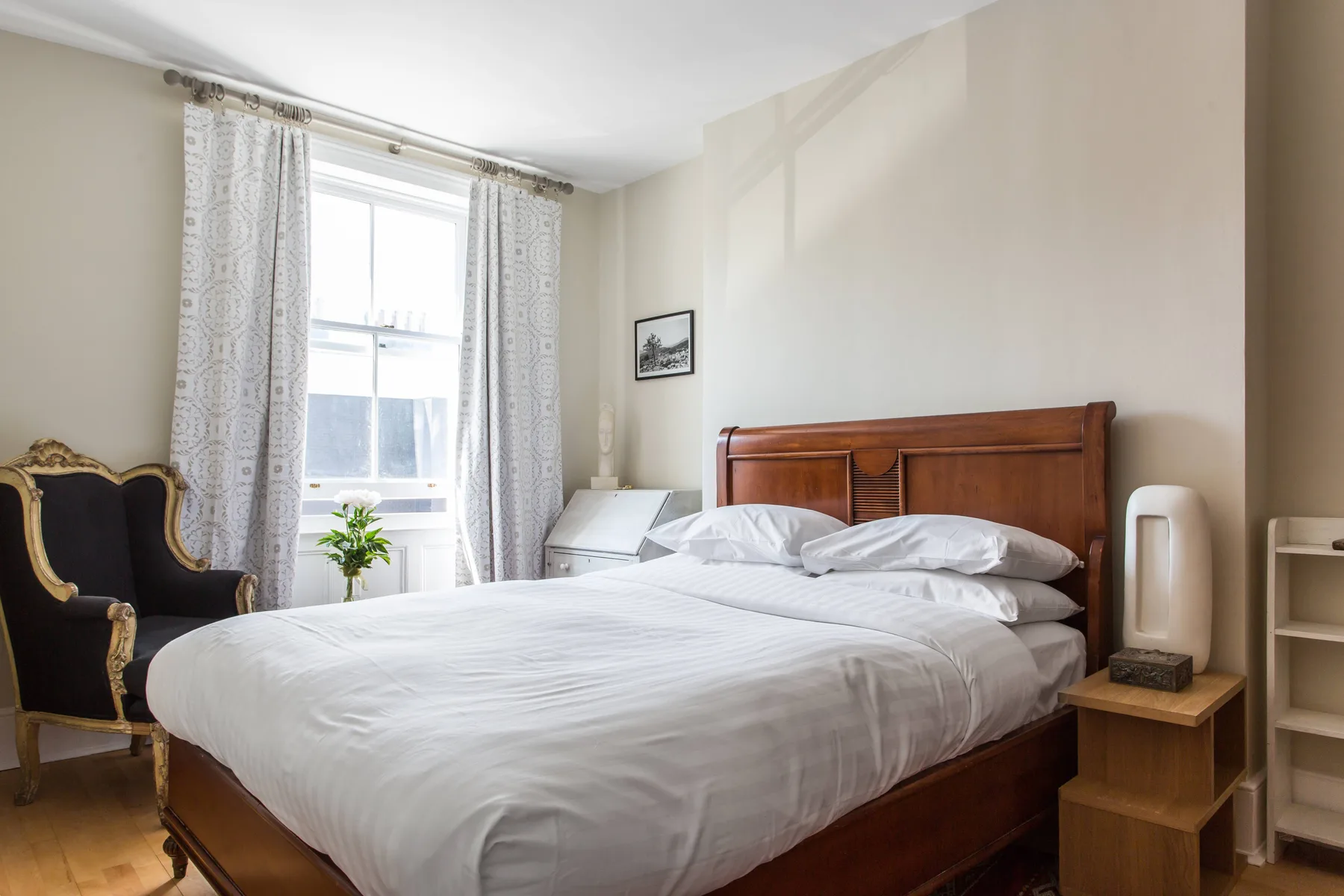 Un dormitorio con una cama grande, una ventana luminosa y un sillón tapizado.