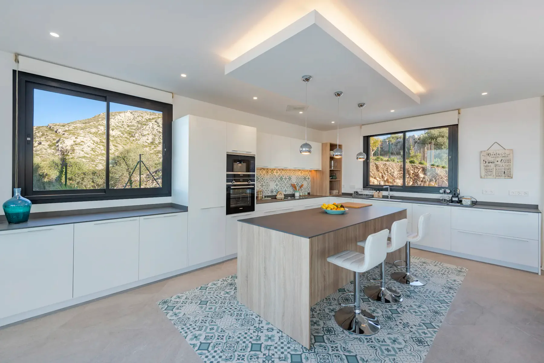 A bright modern kitchen with a central island and wide windows overlooking a hillside.