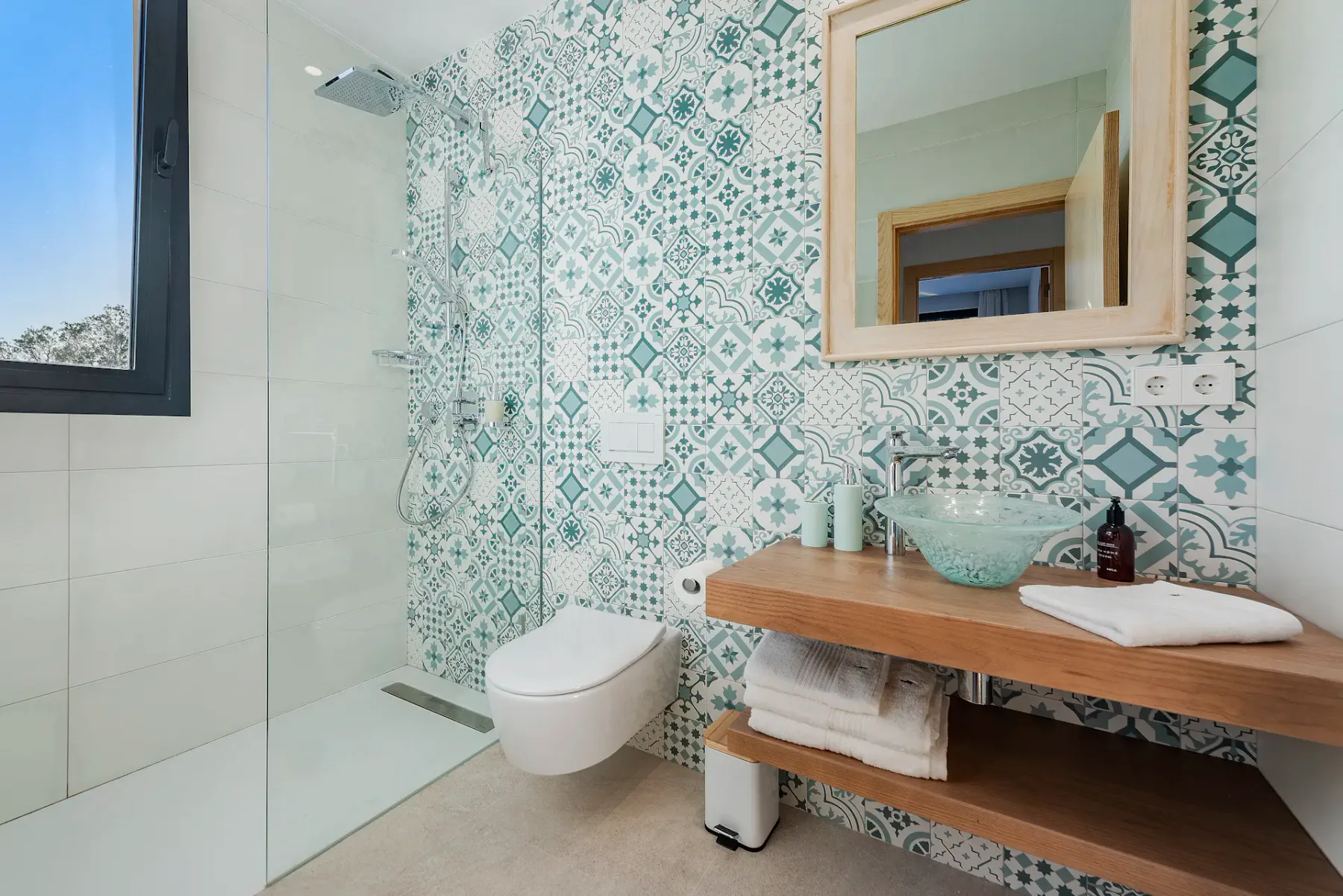 A bathroom with a glass shower, patterned tile, and a wooden vanity.
