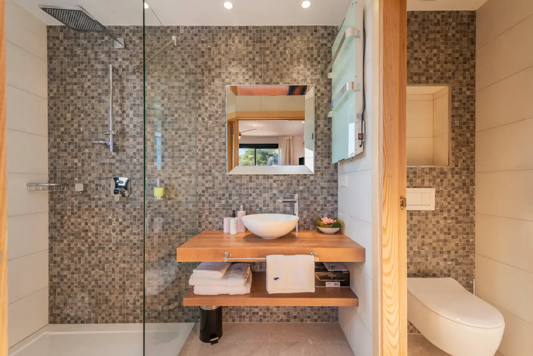 A bathroom with a glass shower, tiled walls, and a vanity.