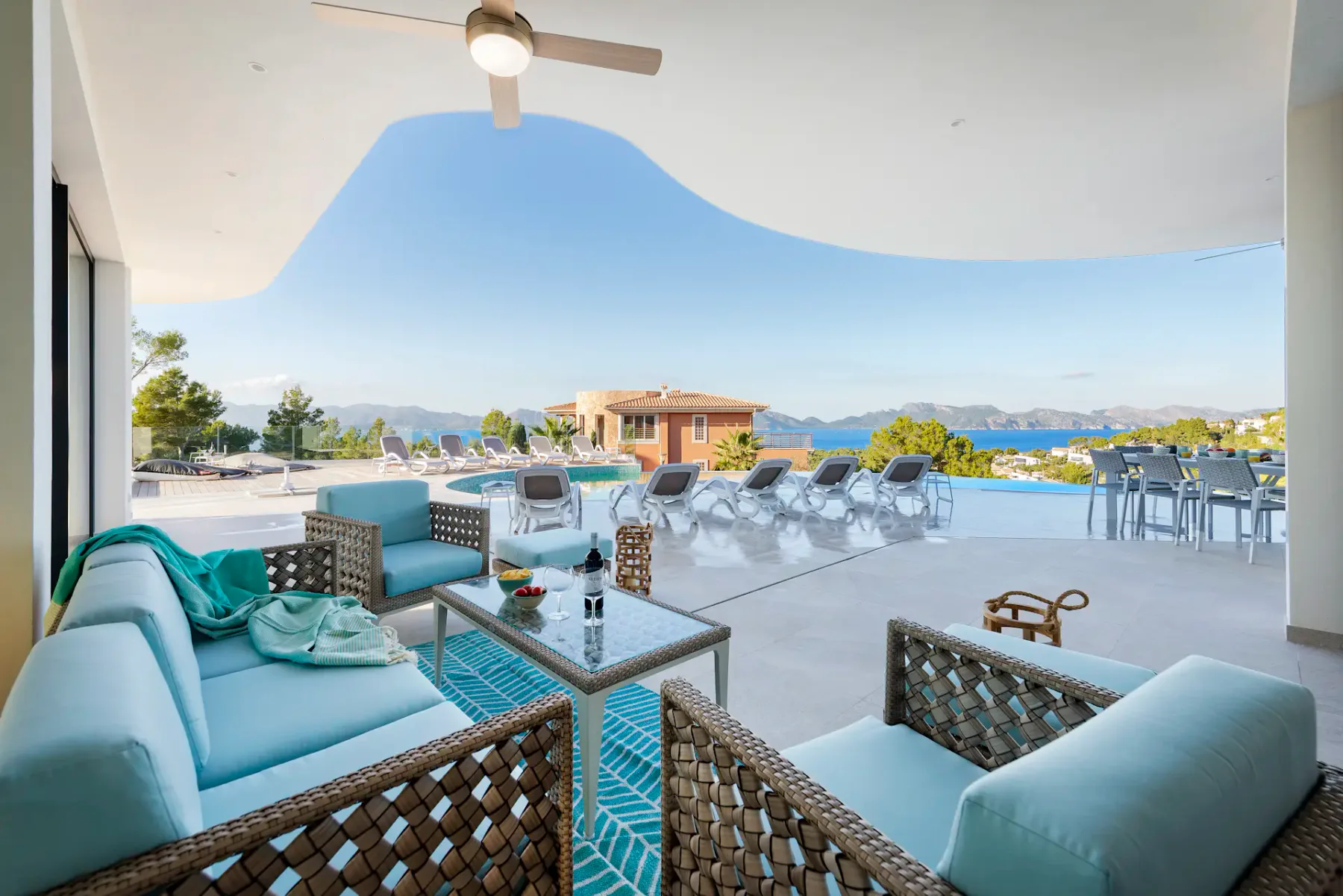 A covered terrace with seating overlooks a pool and distant sea.