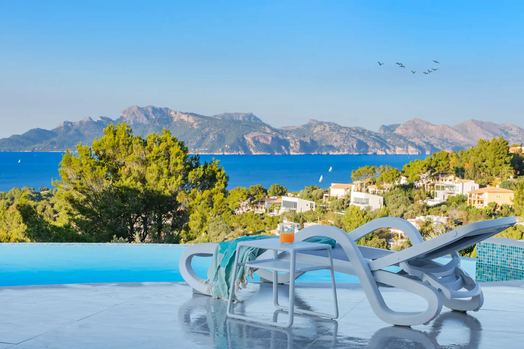 A swimming pool overlooks the sea, with lounge seating in the foreground.
