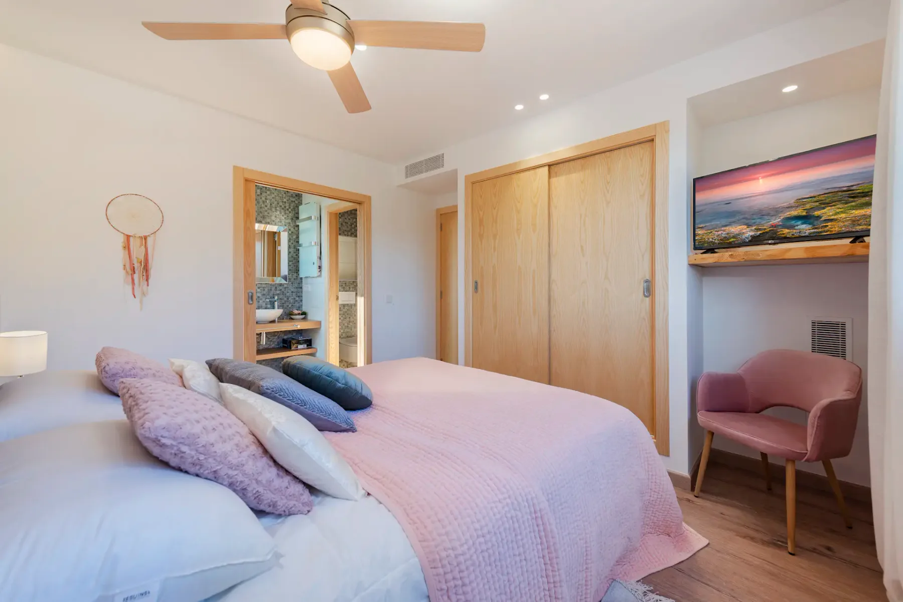 A bedroom with a bed, wooden closet doors, and a pink chair.
