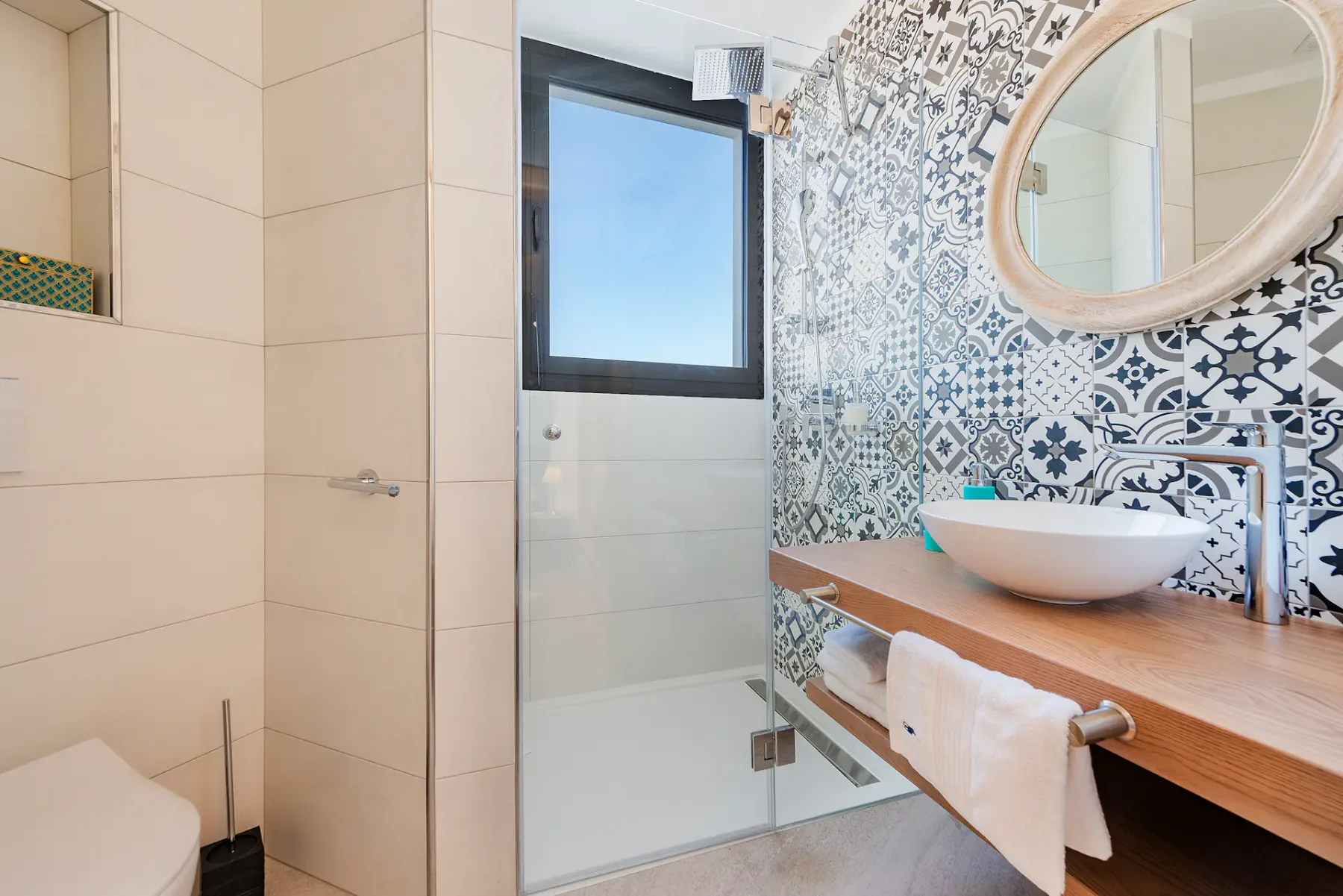 A bathroom with a glass shower, patterned tile, and a wood vanity.