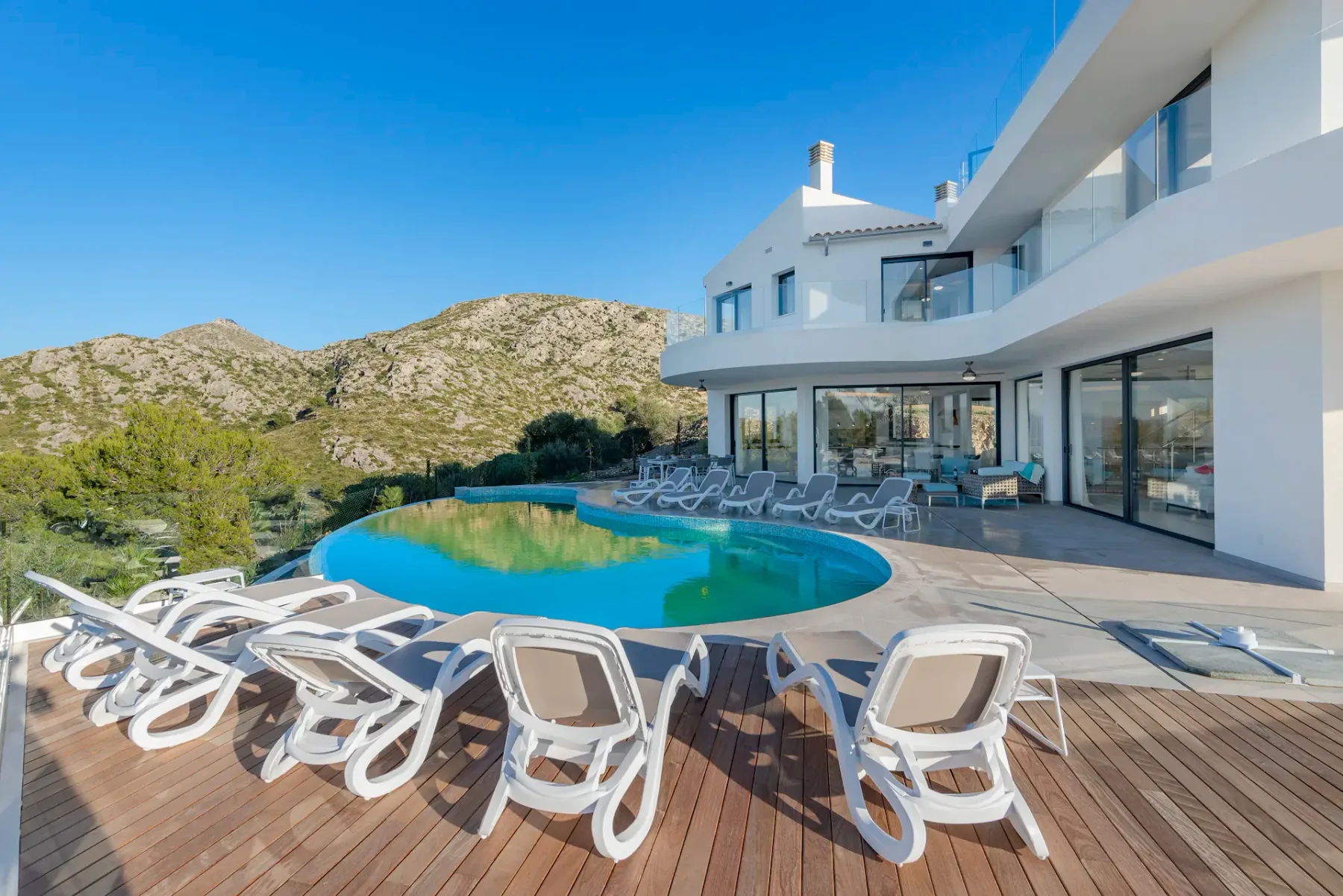 An outdoor swimming pool beside a modern white building, with loungers on the deck.