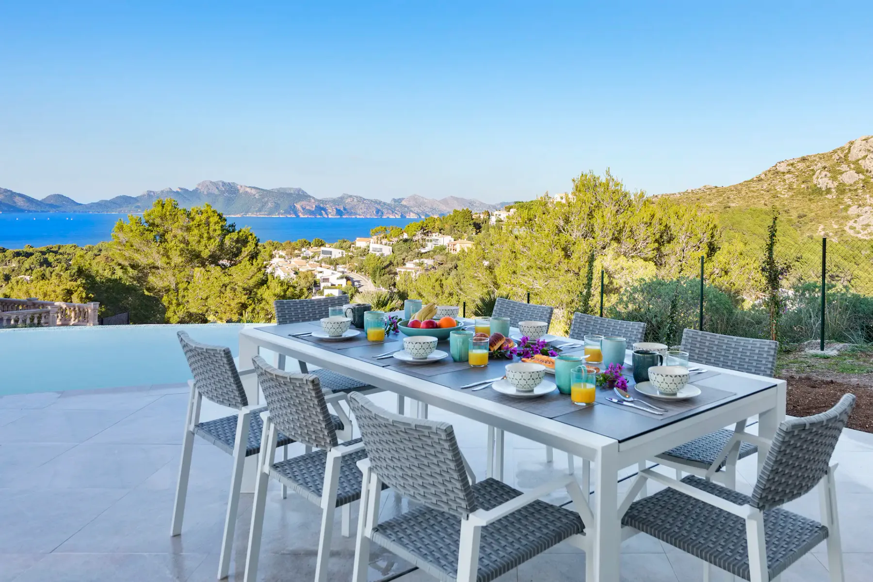 An outdoor dining table and seating overlook the sea and surrounding hills.