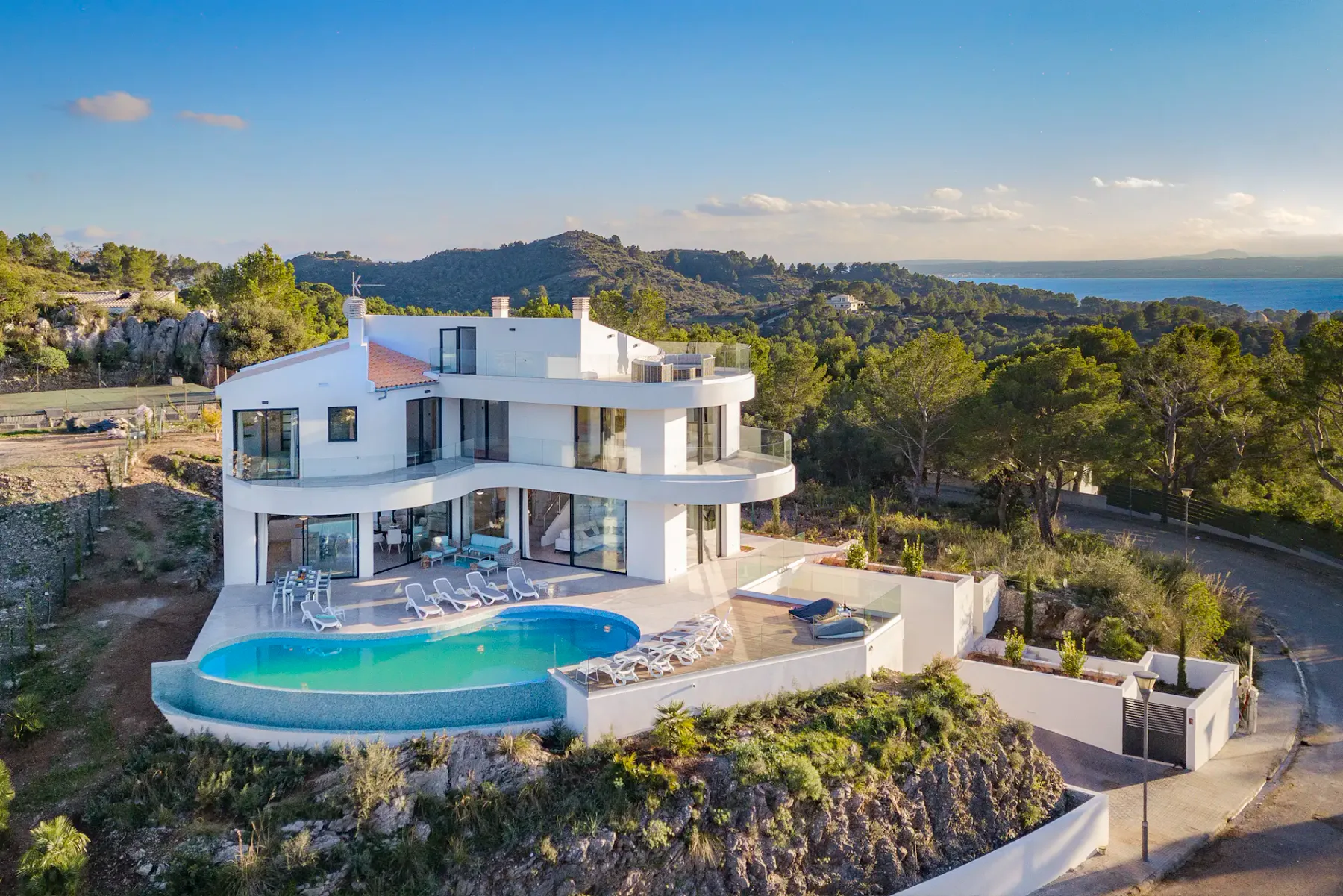 A modern villa overlooks a wooded hillside, with a pool and sea visible beyond.