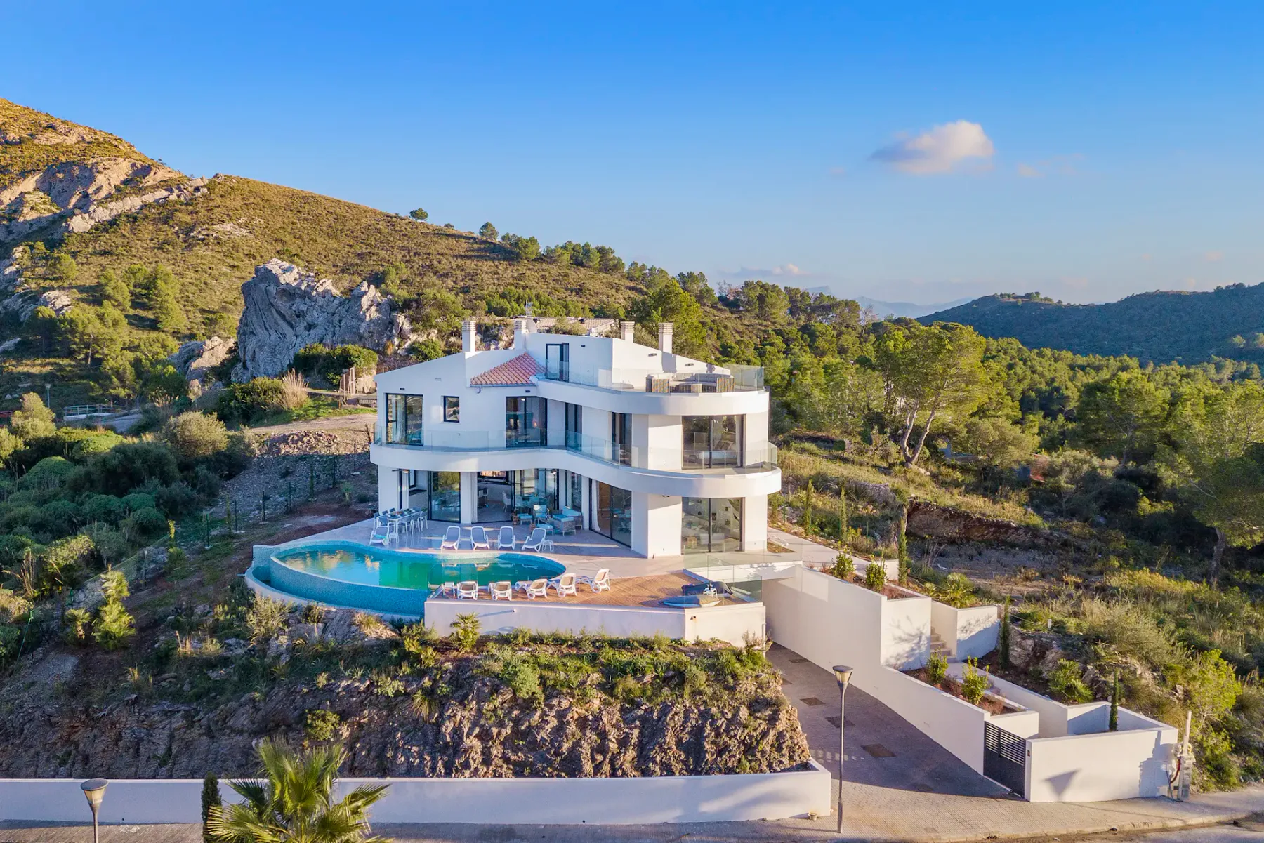 A modern villa with a pool sits among green hills beneath a clear sky.