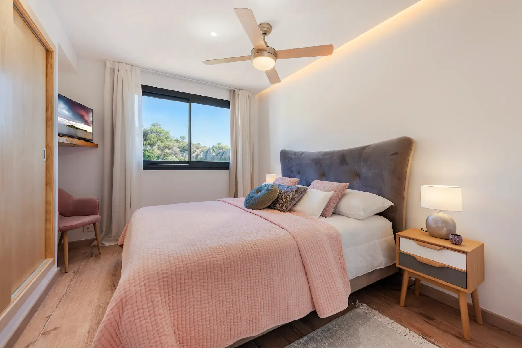A bedroom with a double bed, pink bedding, and a window overlooking trees.