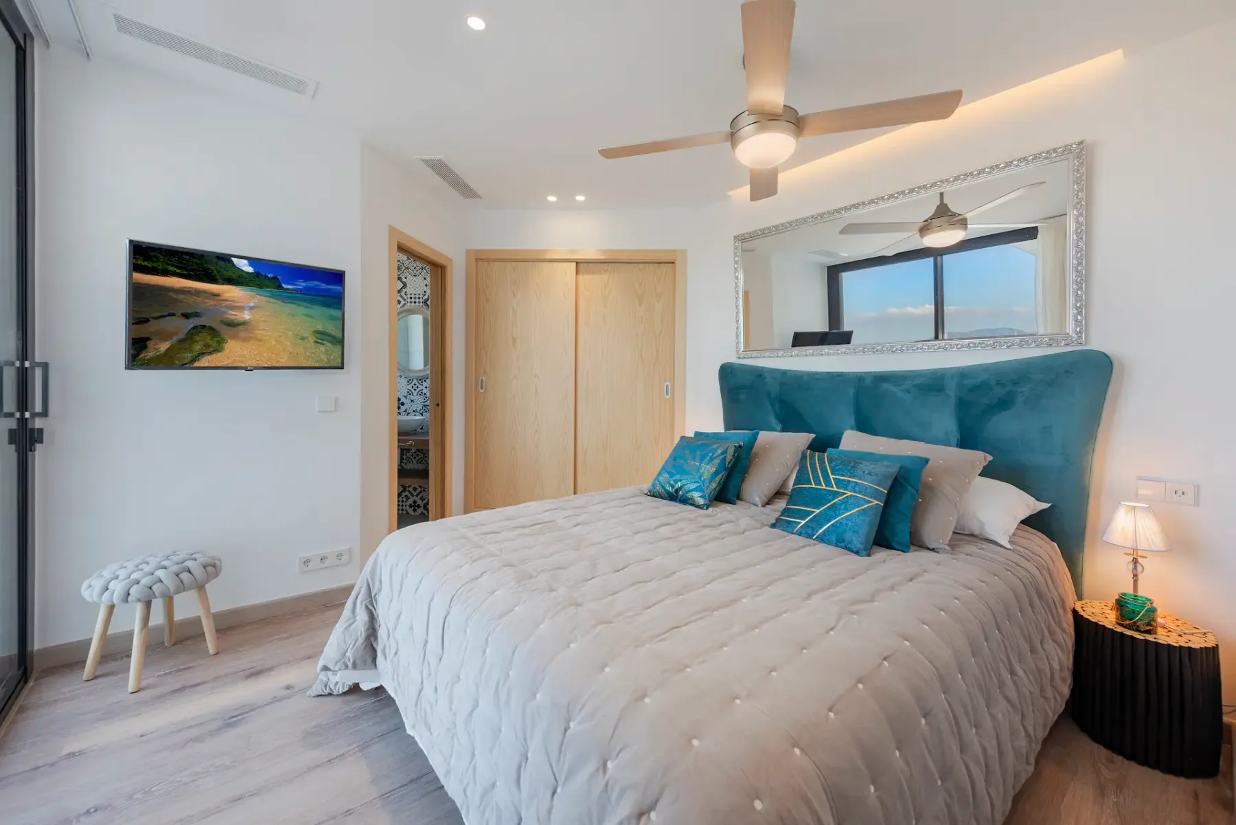 A bedroom with a large bed, teal headboard, and wall-mounted television.