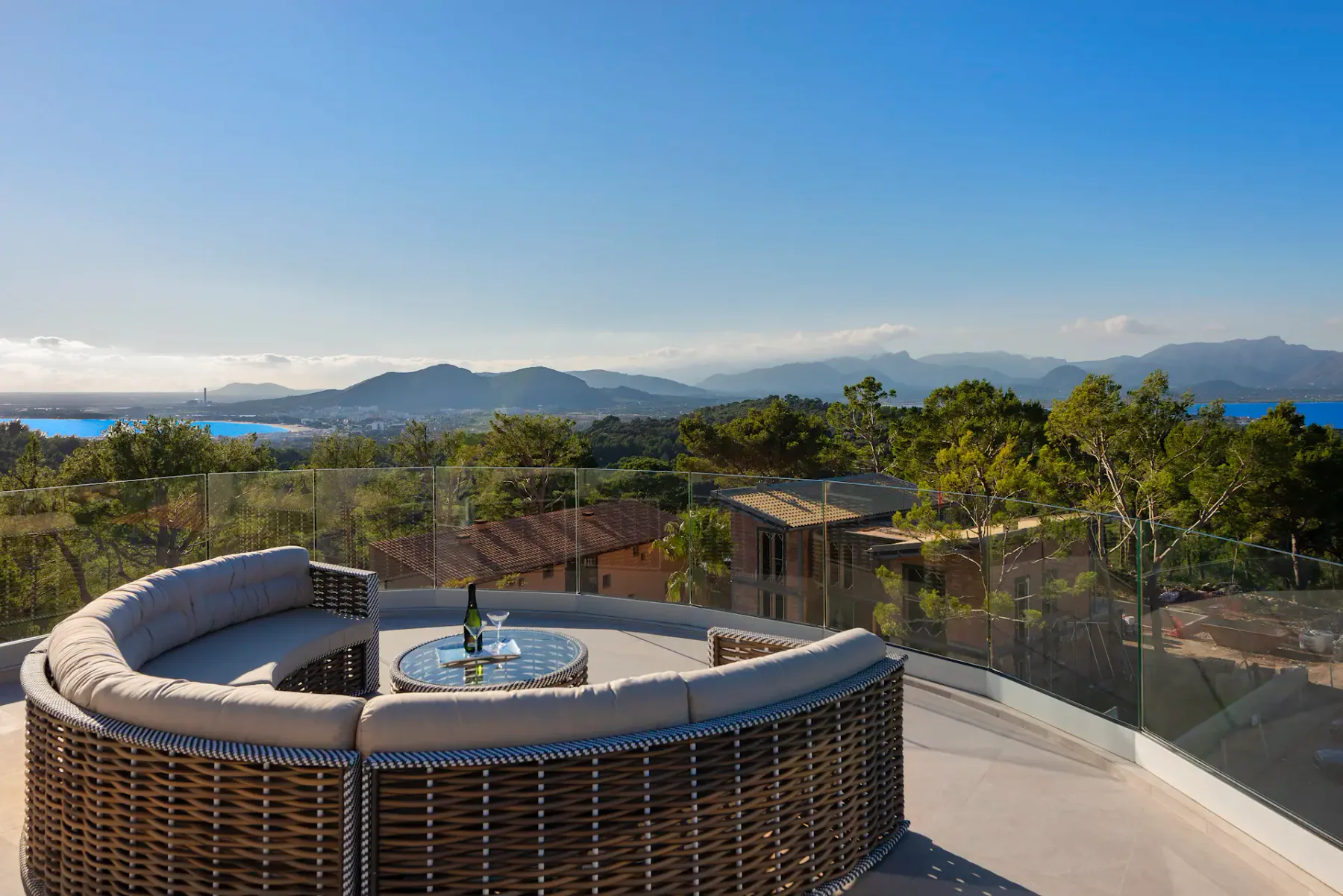 A curved outdoor seating area overlooks a glass railing, trees, and distant mountains.
