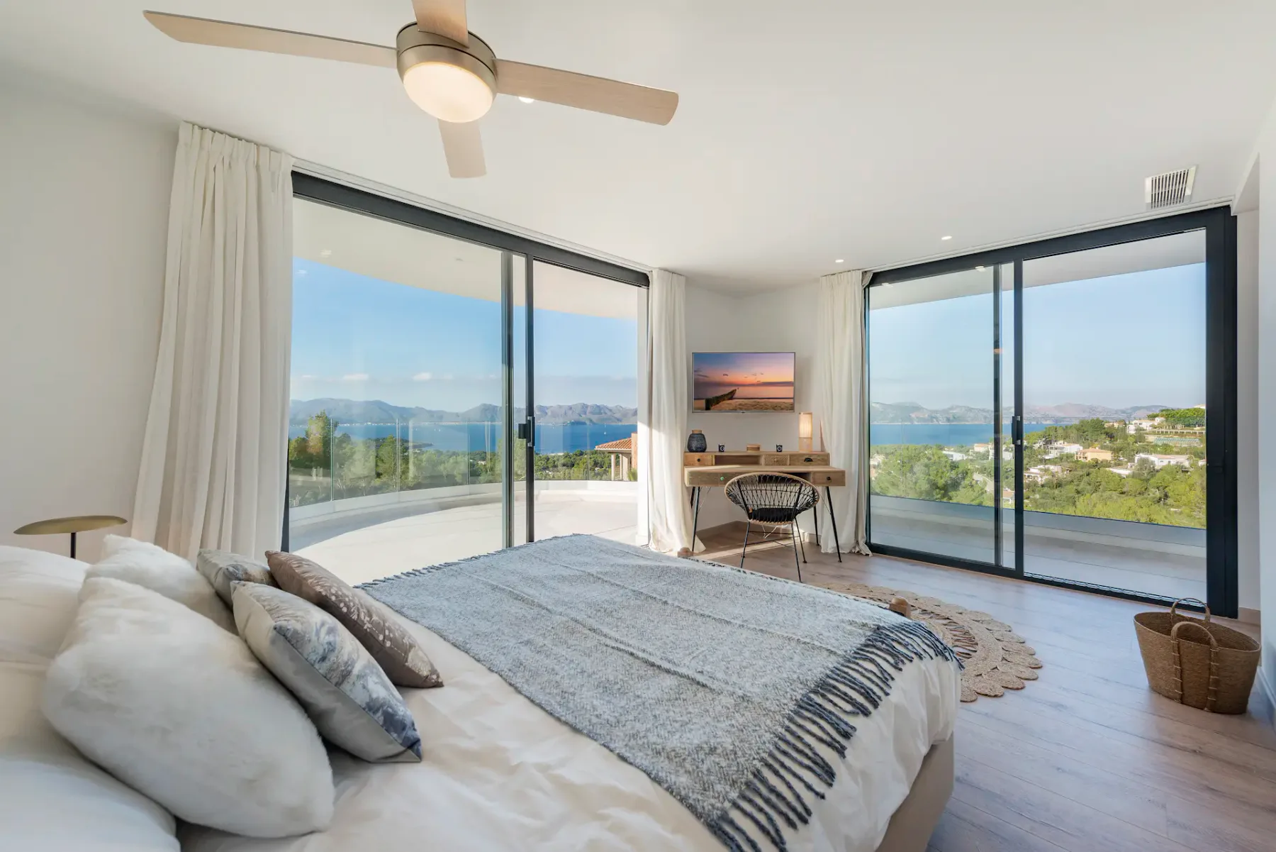 A bright bedroom with a bed and broad windows overlooking the sea.