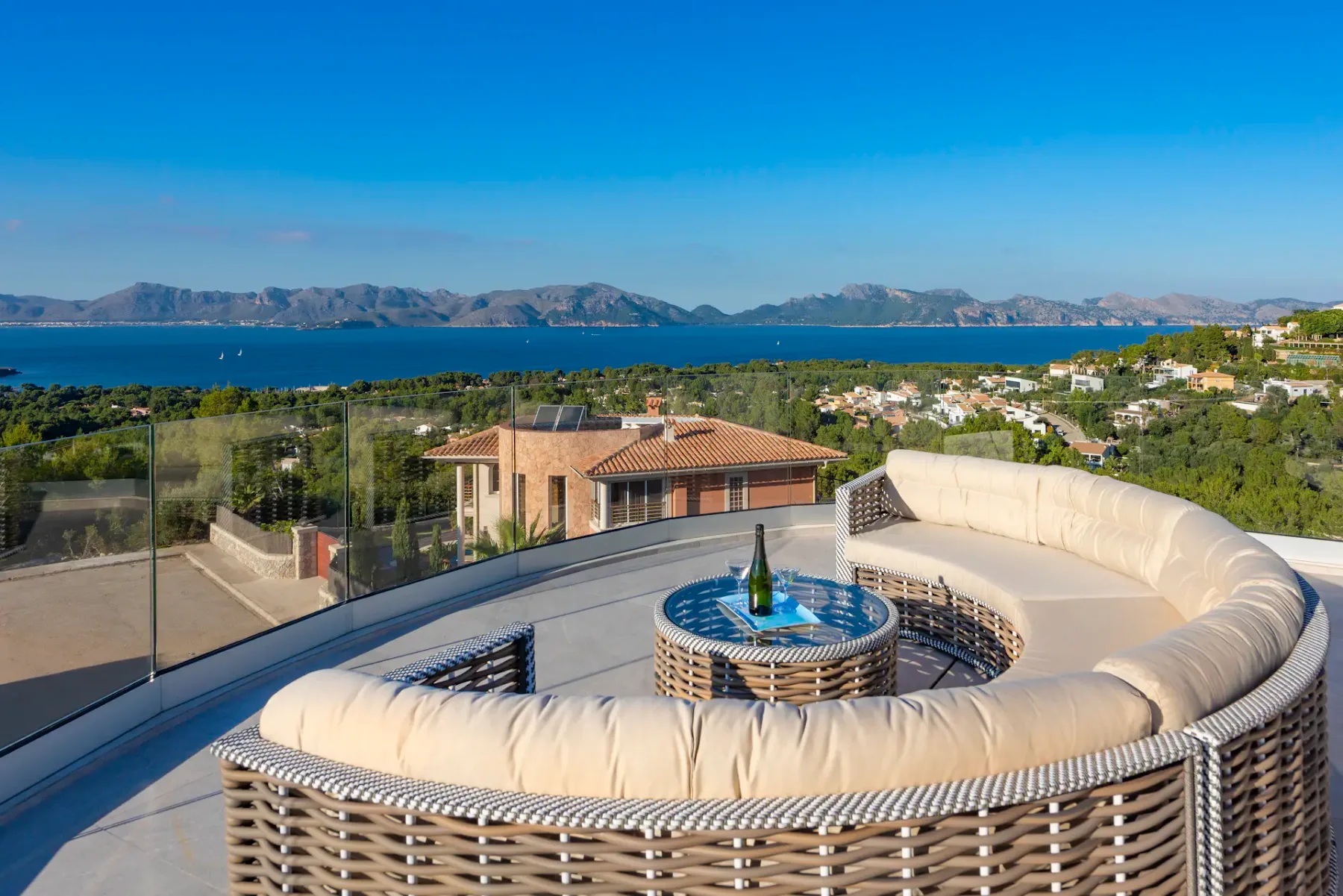 A rooftop terrace has curved seating and a glass railing overlooking the sea.