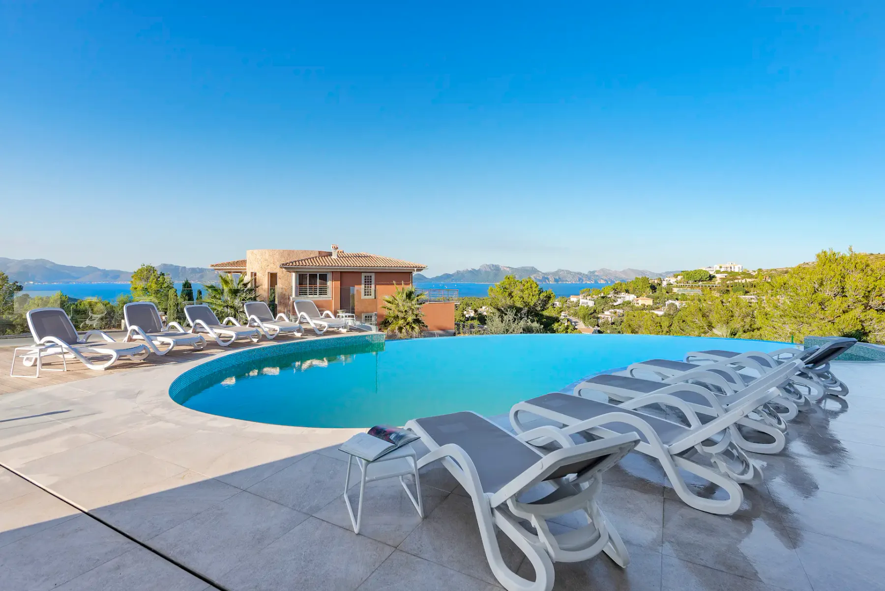 An outdoor swimming pool is surrounded by lounge chairs, with the sea visible beyond.