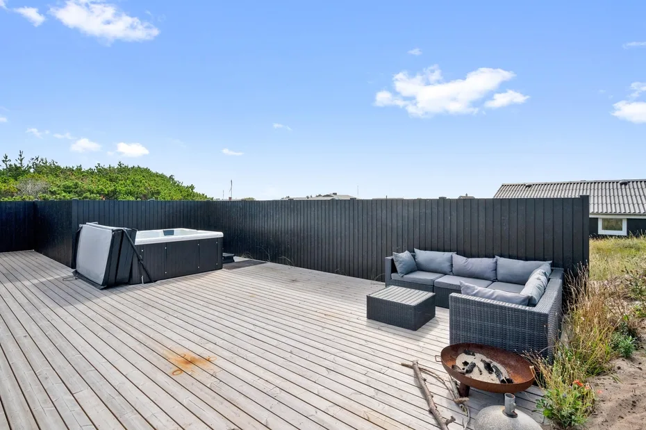 Una terraza exterior tiene una bañera de hidromasaje, asientos acolchados y un brasero.