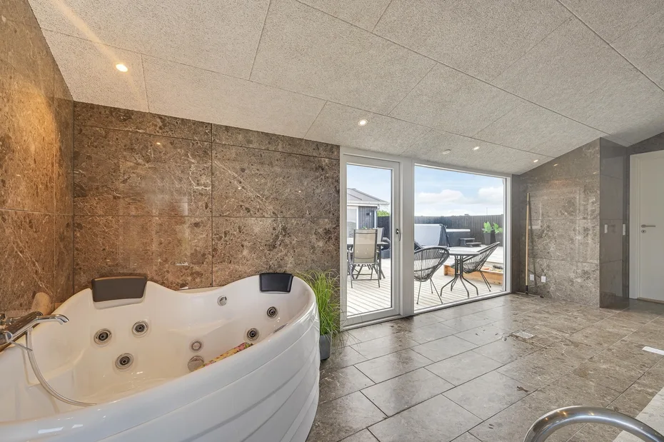 Baño de azulejos con una gran bañera de hidromasaje junto a puertas de vidrio que dan a un patio.
