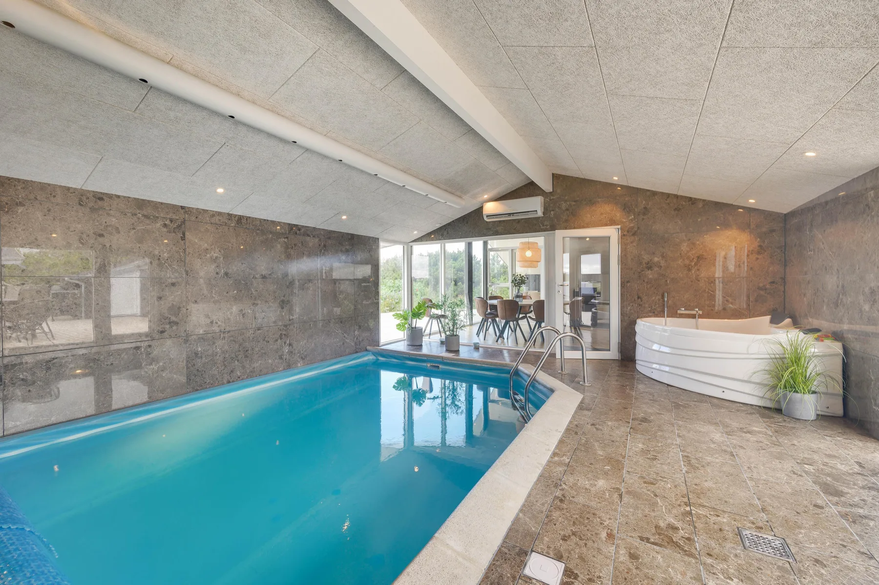 Una piscina cubierta junto a una zona de estar y una bañera grande.
