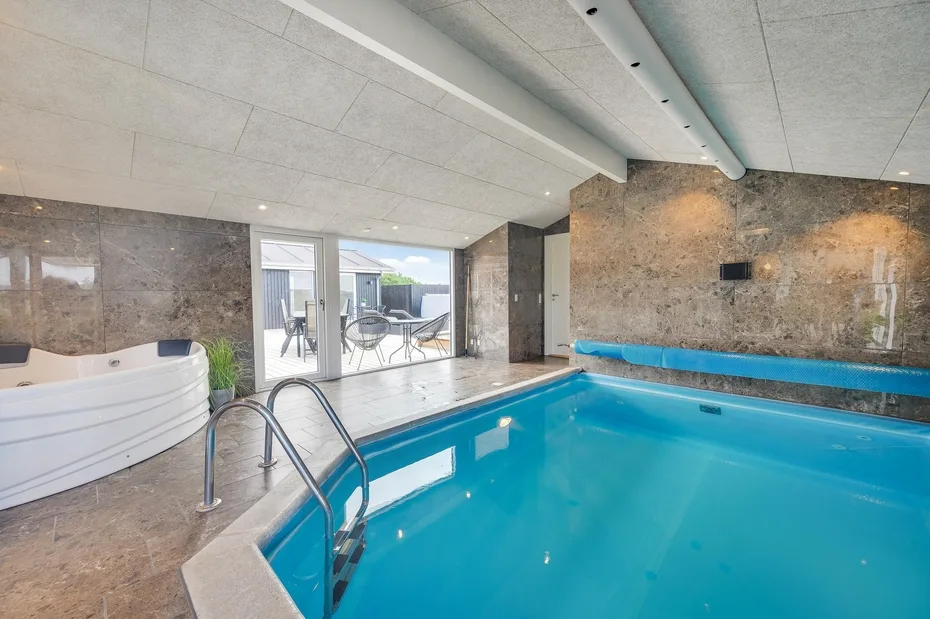 Una piscina cubierta con una bañera de hidromasaje y puertas de vidrio hacia un patio.