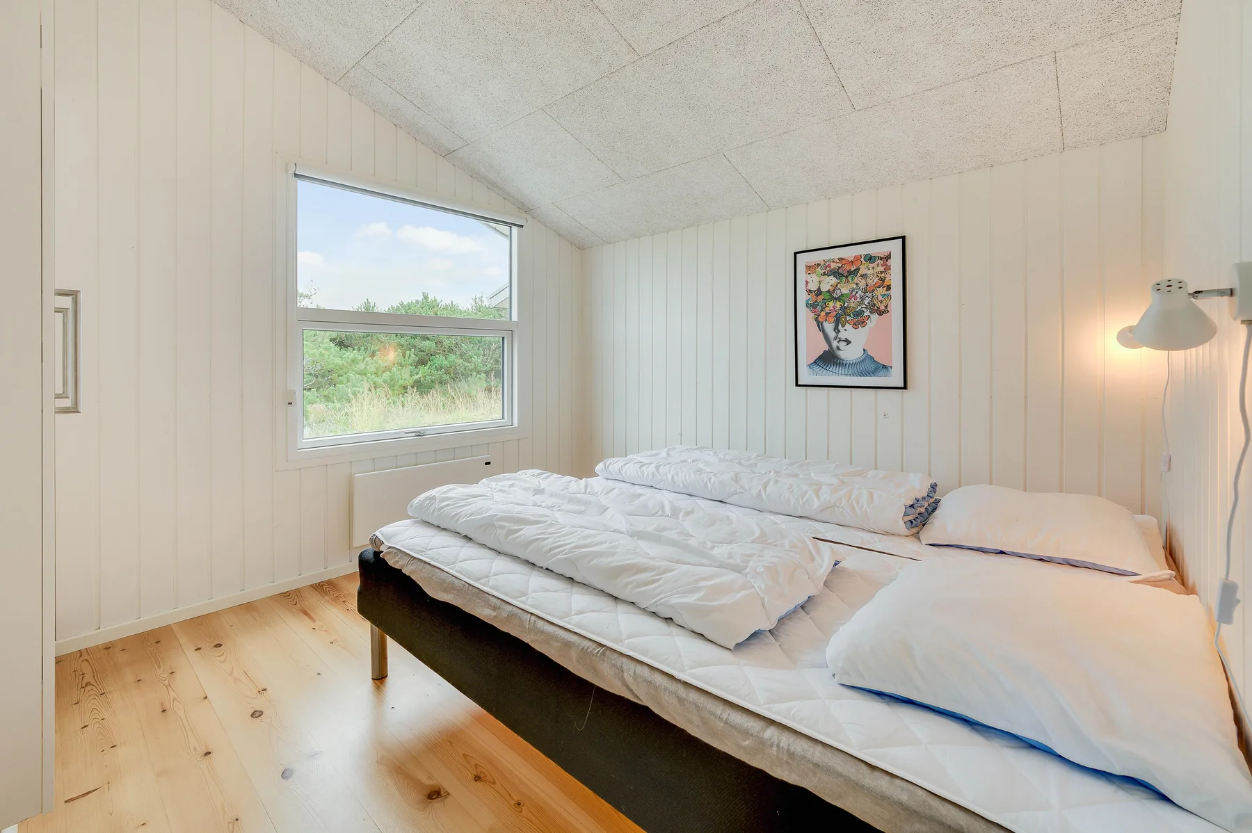 Un dormitorio luminoso con ropa de cama blanca y una ventana con vistas a la vegetación.