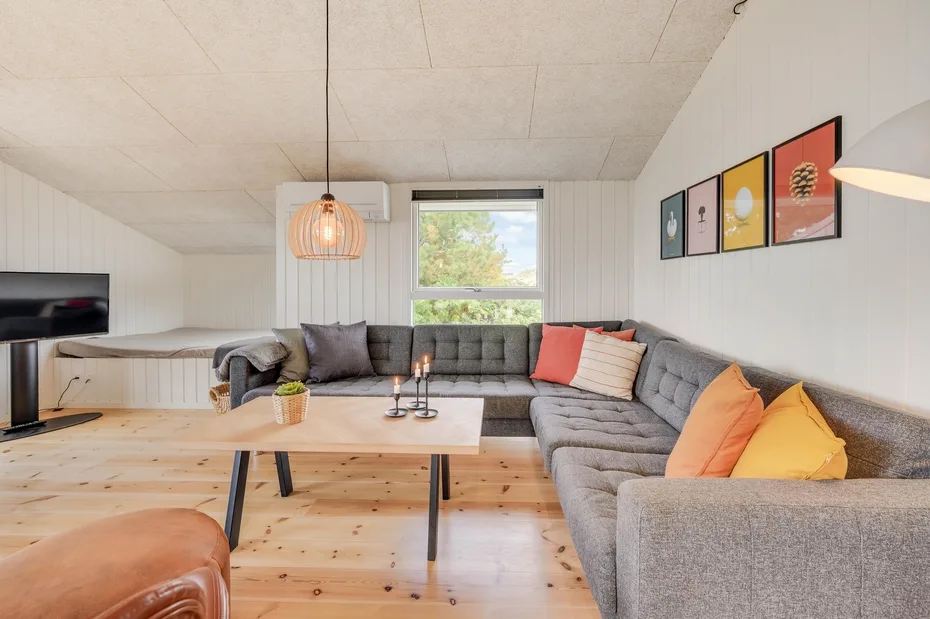 Una sala luminosa cuenta con un sofá seccional gris, una mesa de centro de madera y una ventana amplia.