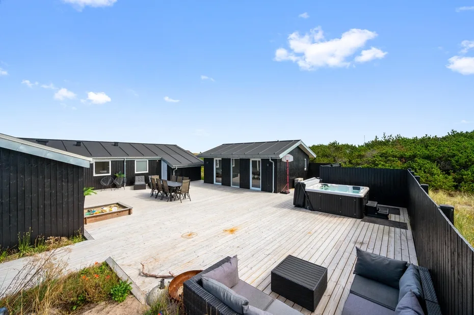 Una amplia terraza de madera con asientos al aire libre y una bañera de hidromasaje junto a una casa moderna.