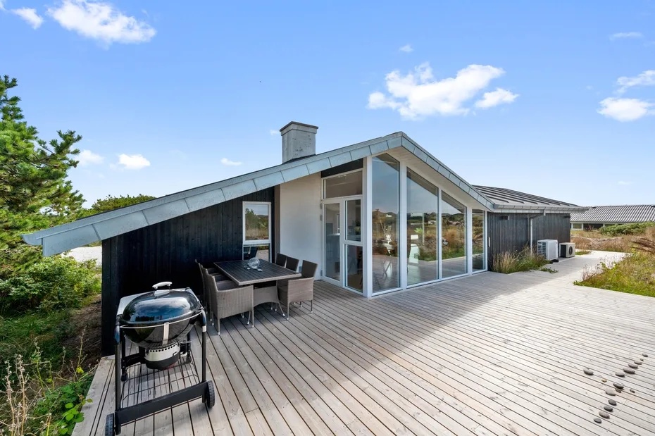 Una casa moderna da a una amplia terraza de madera con asientos al aire libre.