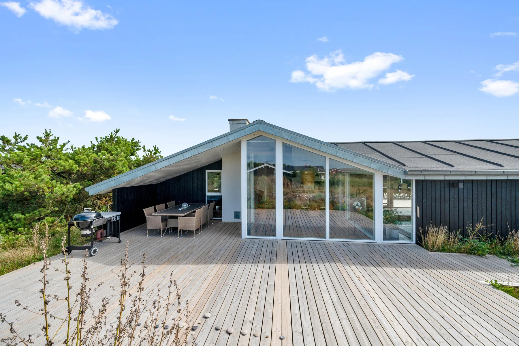 Una casa moderna se abre a una amplia terraza de madera con asientos al aire libre.