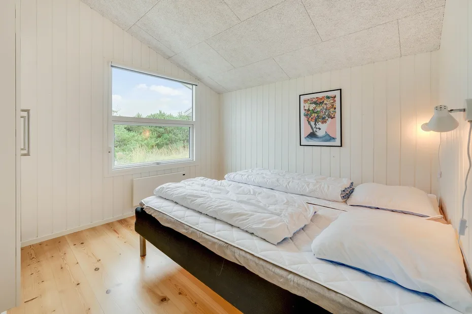 Un dormitorio luminoso con ropa de cama blanca, una ventana y un cuadro en la pared.