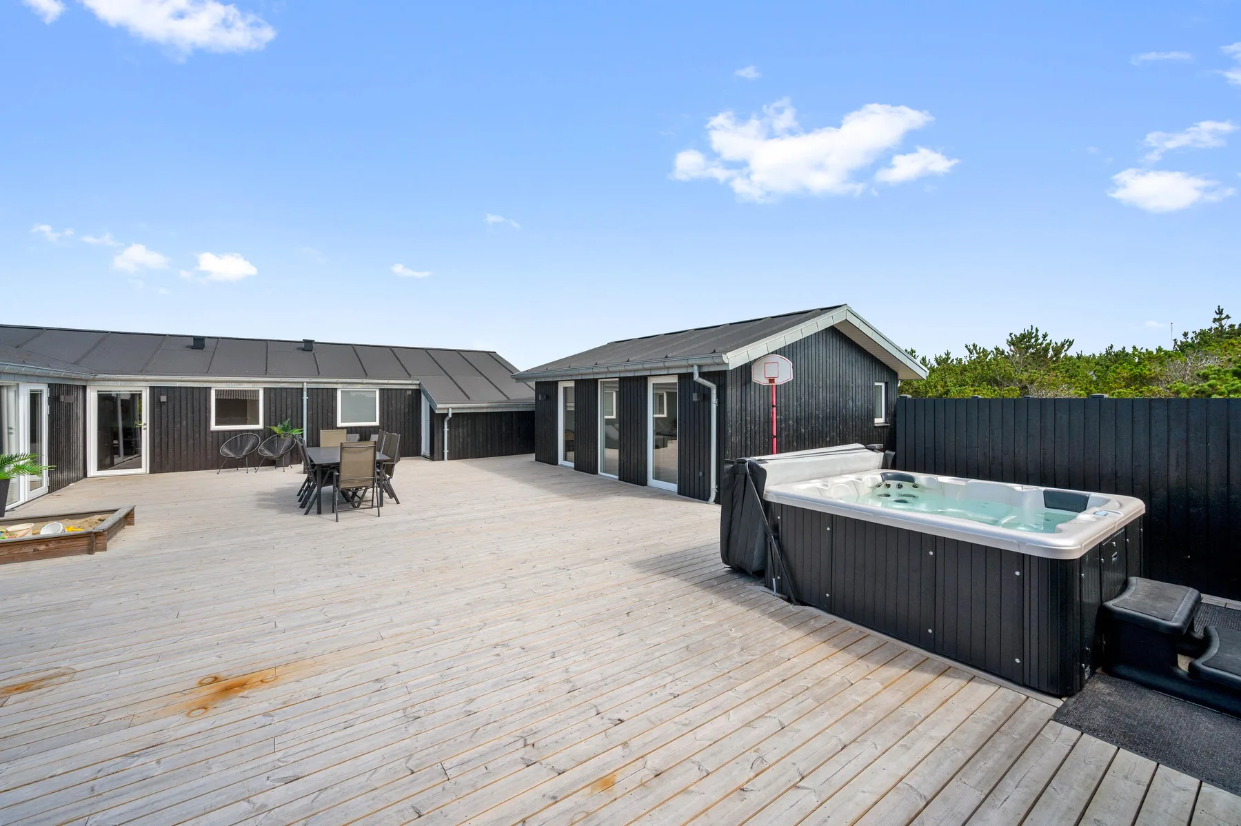 Una amplia terraza exterior con asientos y una bañera de hidromasaje junto a una cabaña oscura.