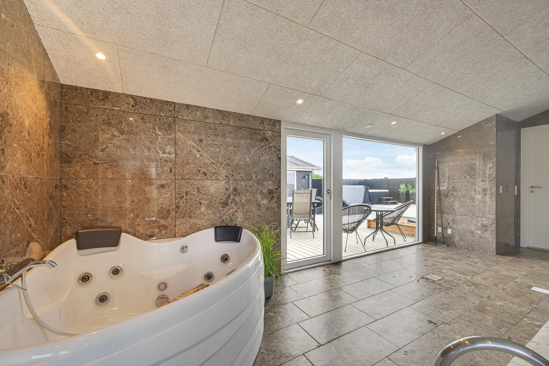 Un baño con azulejos y una amplia bañera de hidromasaje junto a puertas corredizas de vidrio hacia un patio.