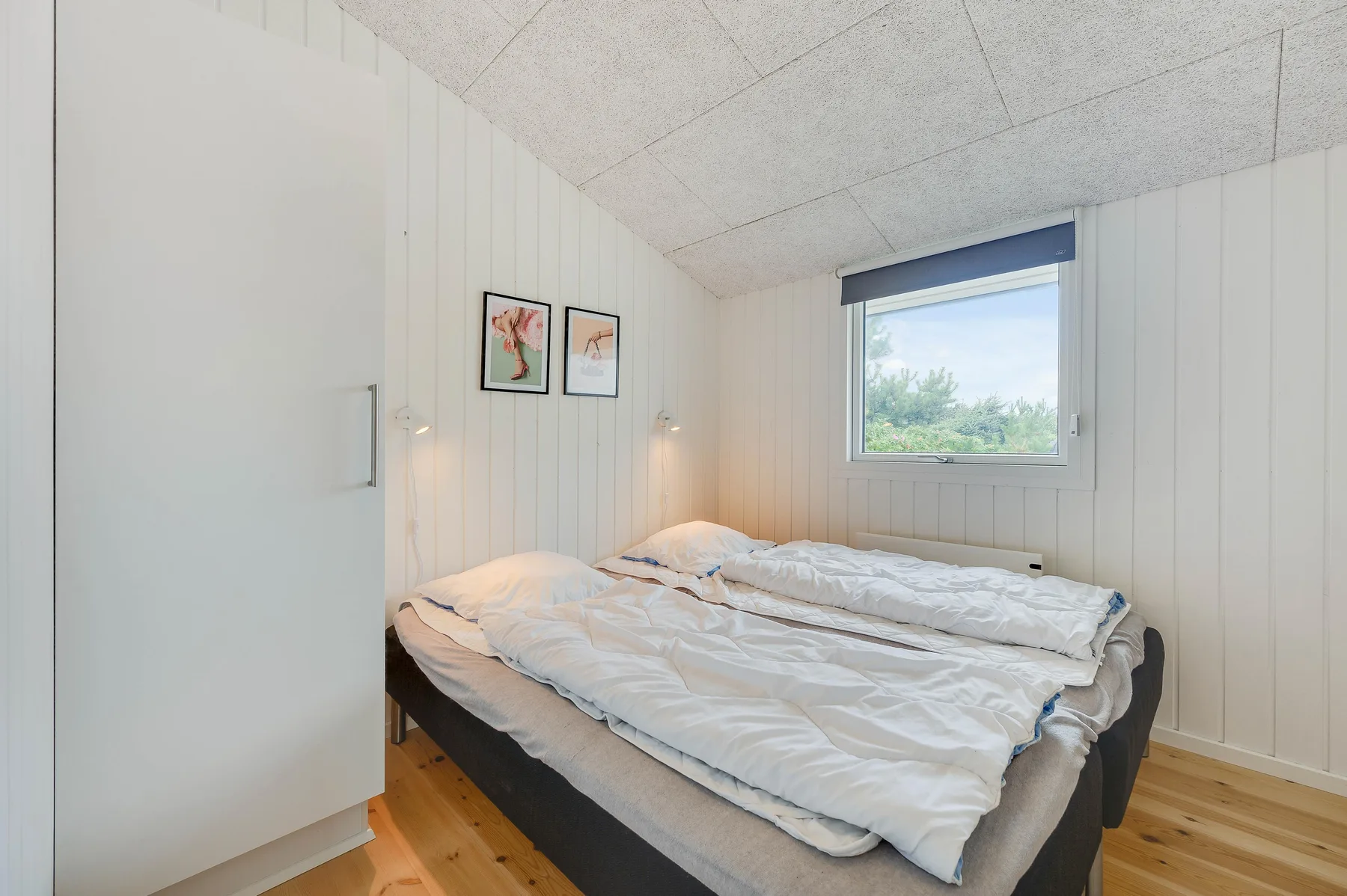 Un dormitorio con una cama doble, ropa de cama blanca y una ventana con vistas a la vegetación.