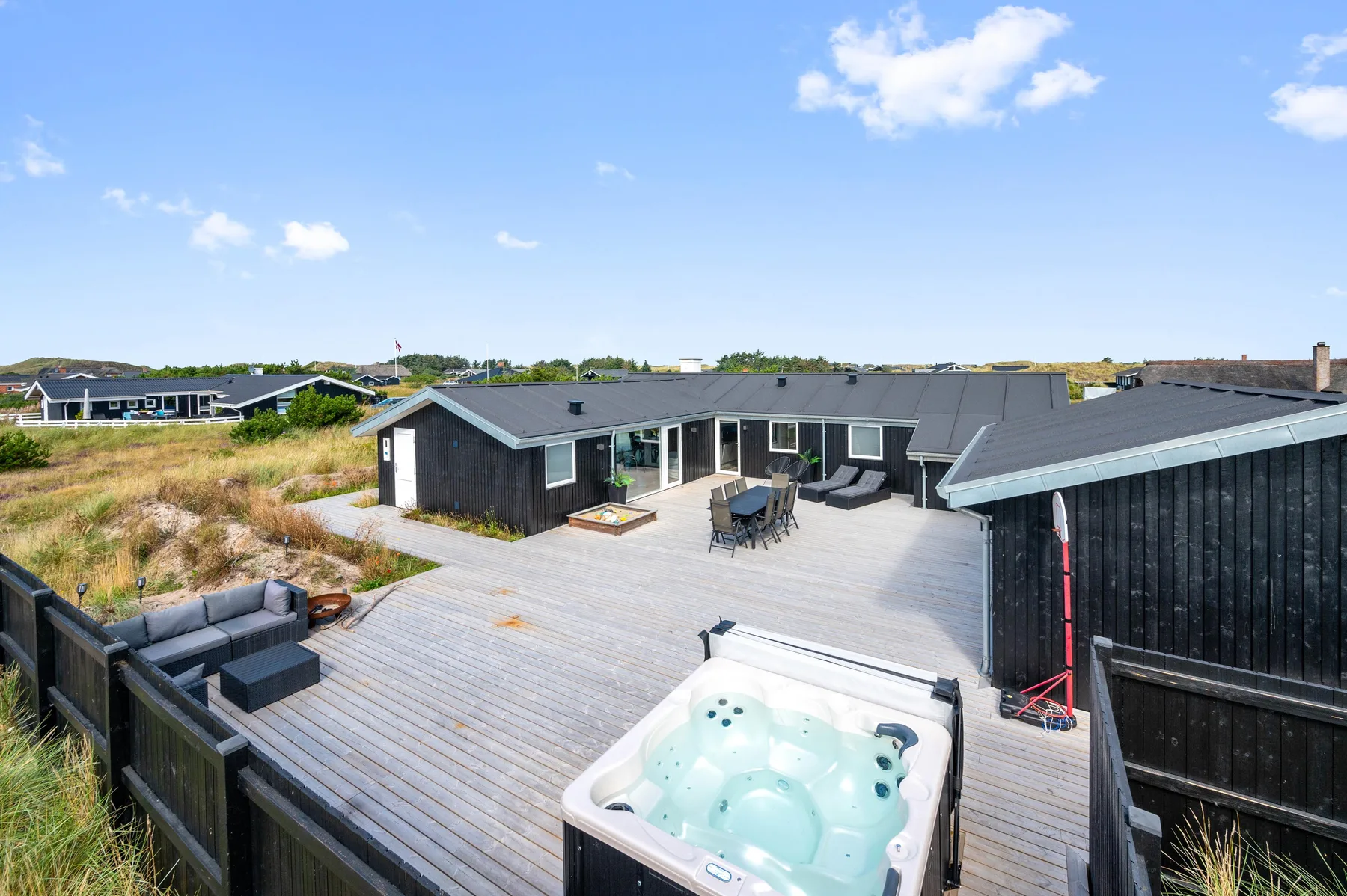 Una casa moderna se abre a una amplia terraza con una bañera de hidromasaje exterior.
