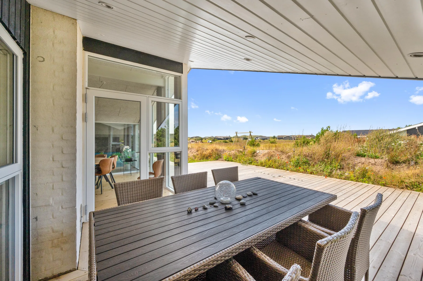 Un patio cubierto tiene una mesa de comedor y asientos con vistas a campos abiertos.