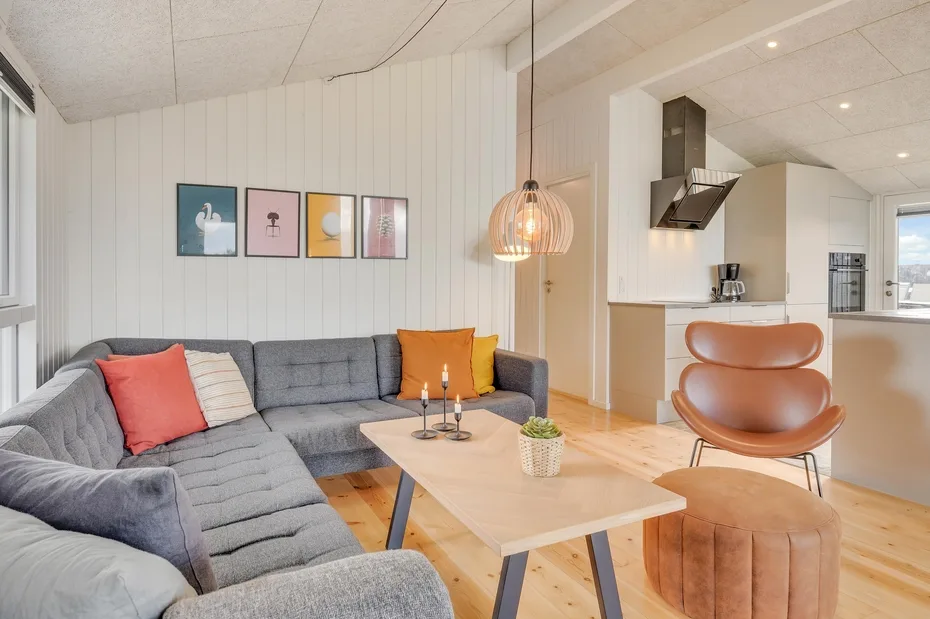 Una sala luminosa con asientos grises, una mesa de centro de madera y una cocina abierta.