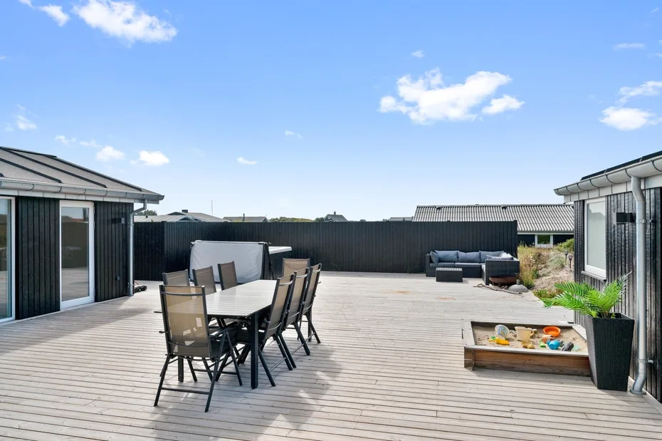 Una amplia terraza exterior tiene asientos de comedor, muebles de descanso y una jardinera elevada.