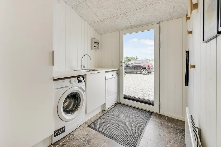 Un cuarto de lavado con lavadora, lavabo y puerta de vidrio hacia una zona de grava.