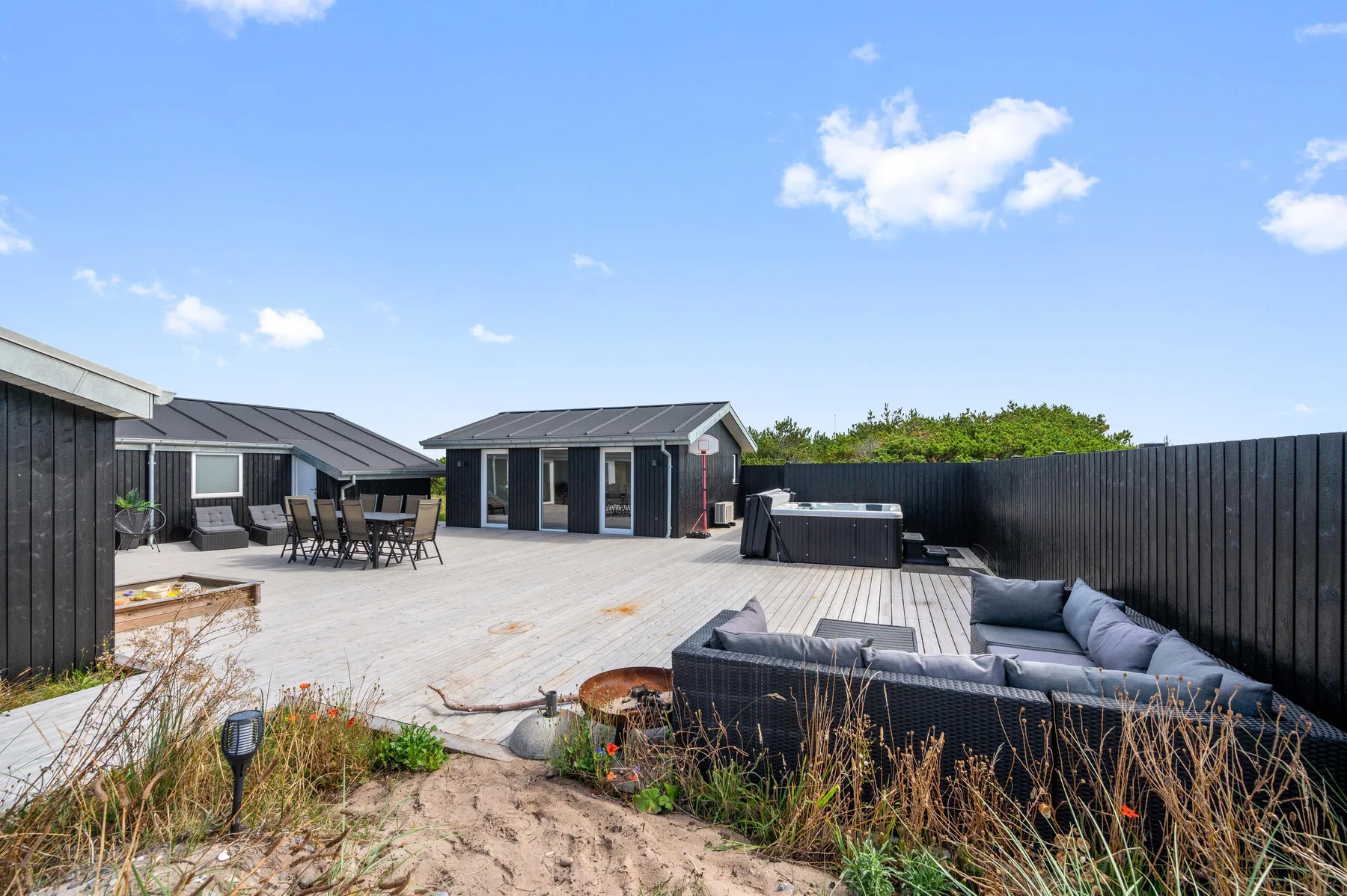 Una amplia terraza exterior con asientos y una bañera de hidromasaje junto a una casa moderna.