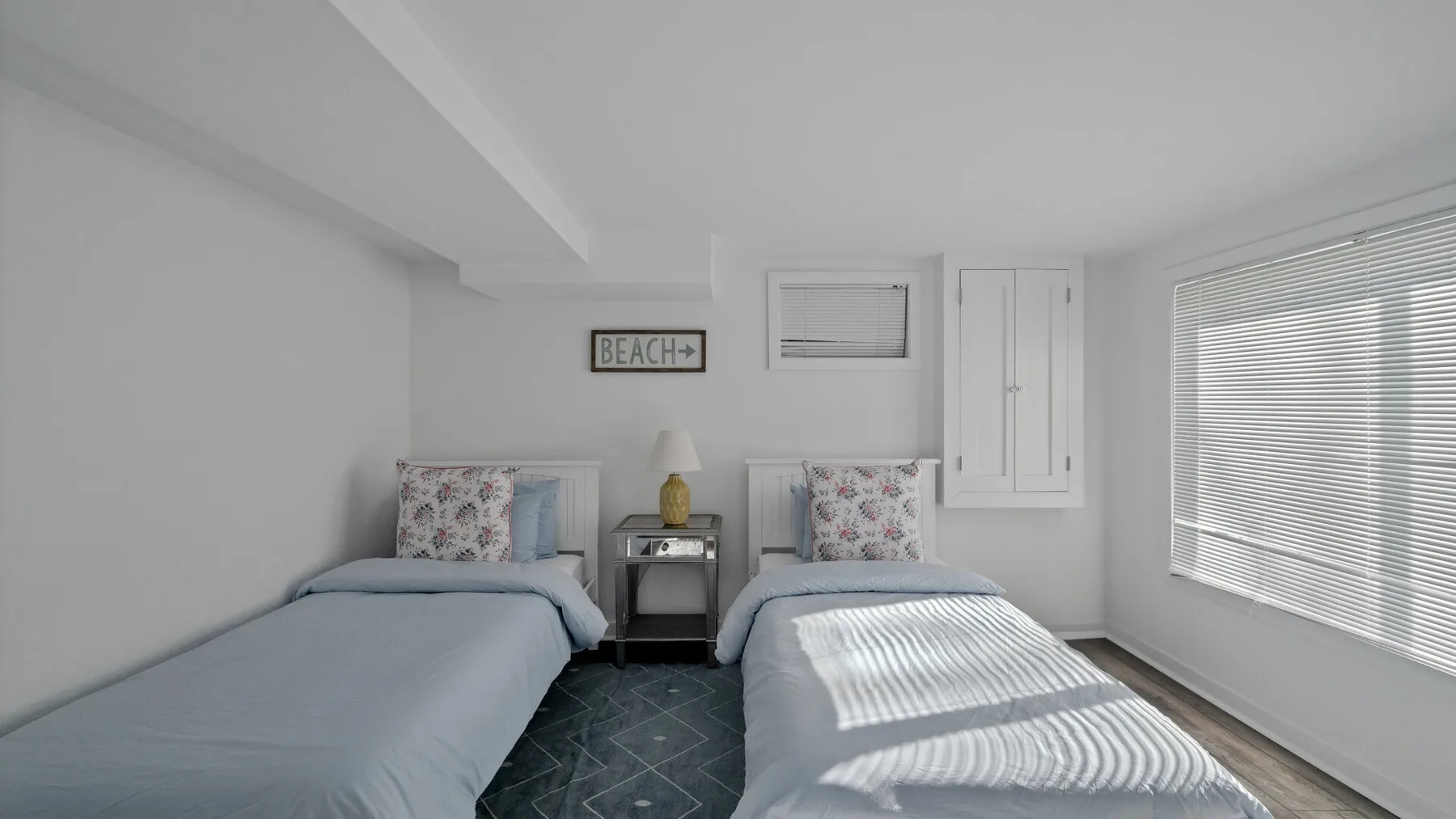 A bright bedroom with two single beds and a large window.