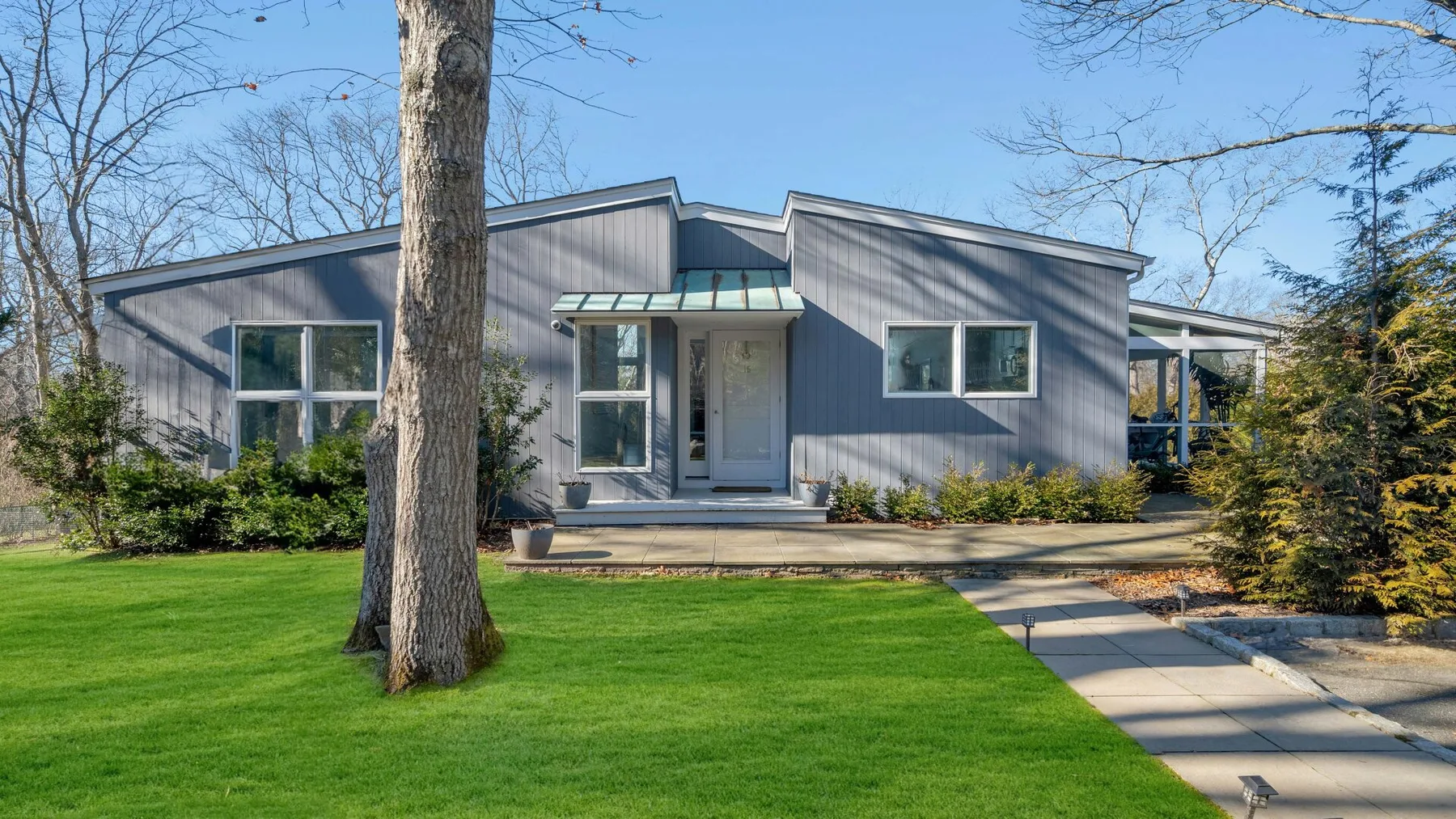 A modern house with a front lawn and a paved walkway leading to the entrance.