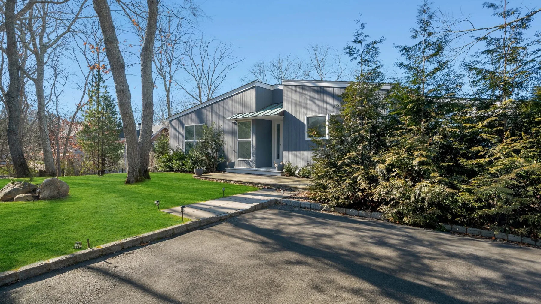 A modern house stands beside a paved driveway and landscaped lawn.