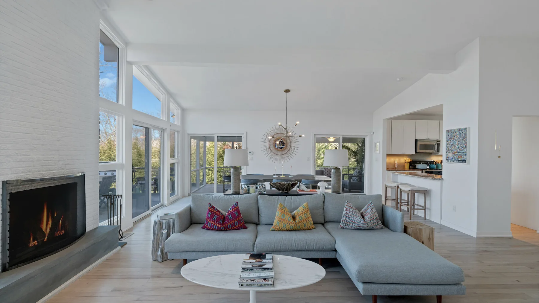 A bright living room has large windows, a fireplace, and sectional seating.