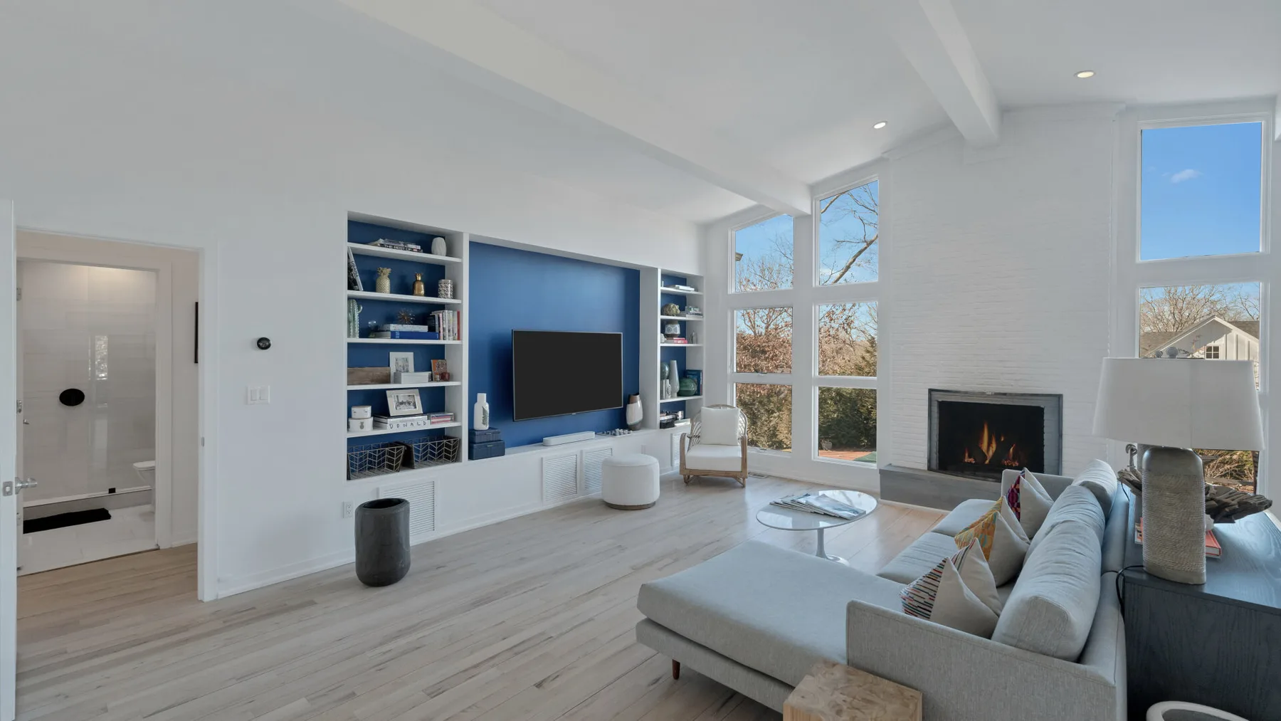 Una sala luminosa con grandes ventanas, un televisor y una chimenea.