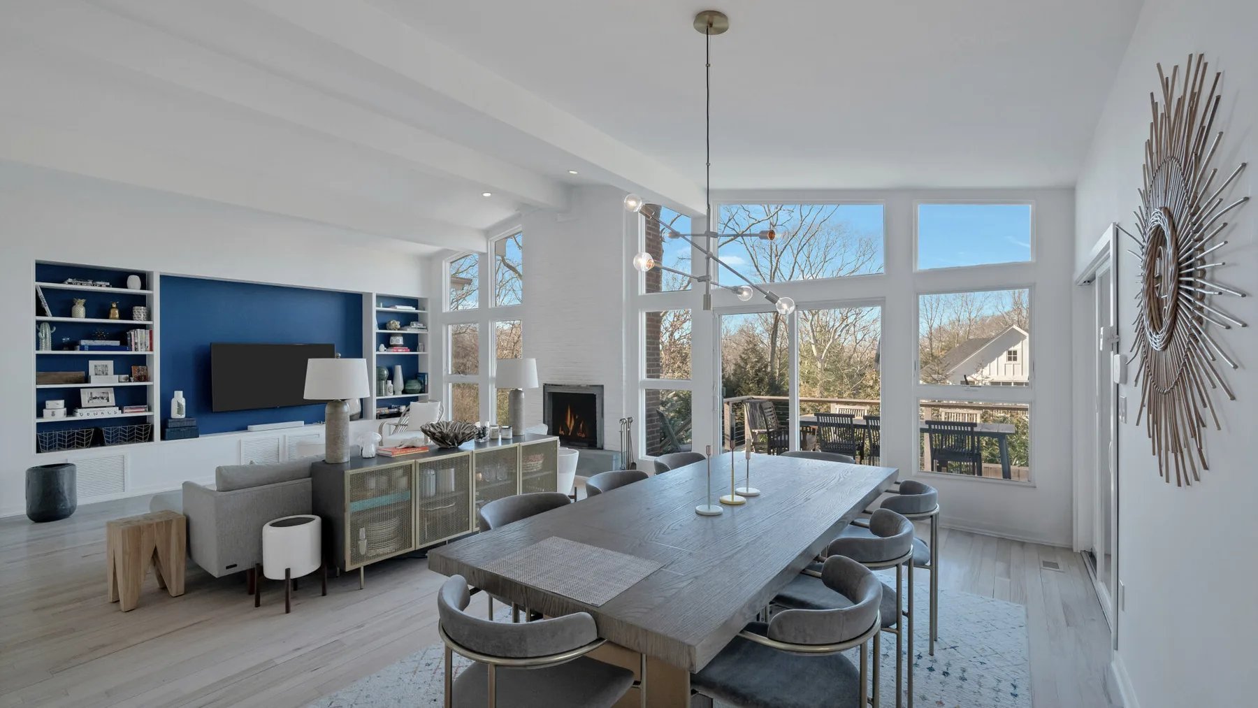 A bright open-plan living and dining area has large windows and a long dining table.