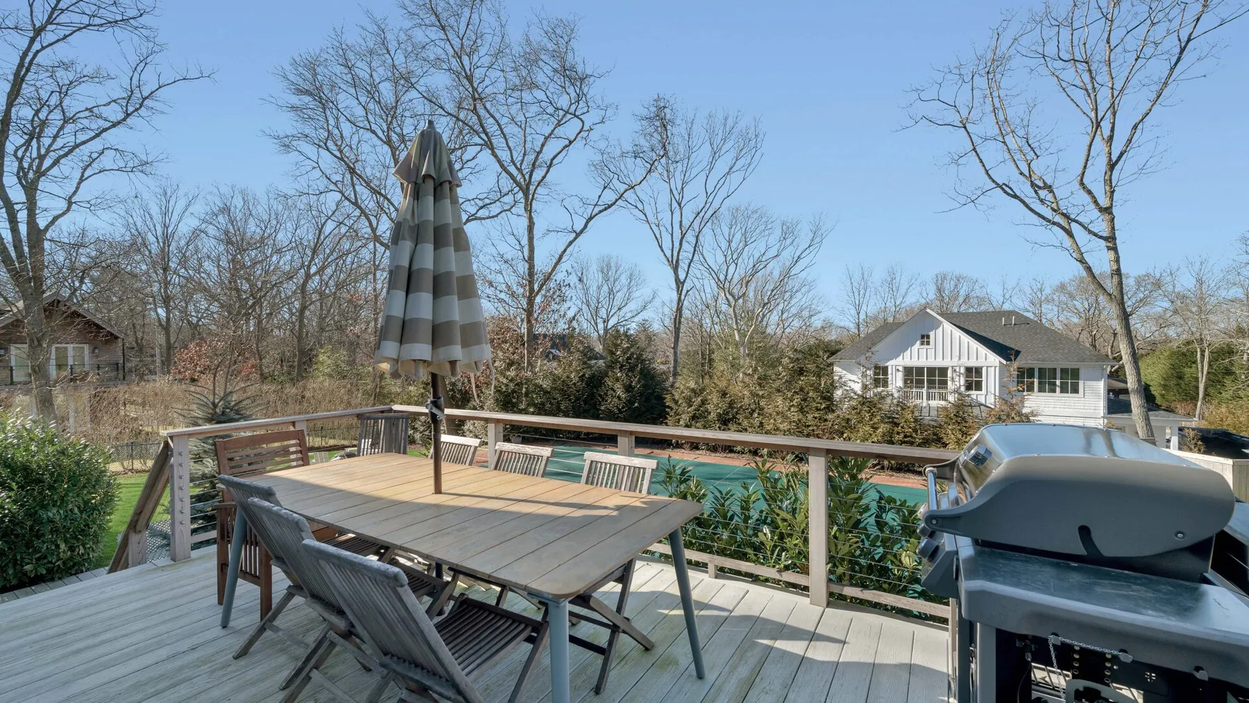 An outdoor deck with a dining table, umbrella, and grill overlooks a swimming pool.