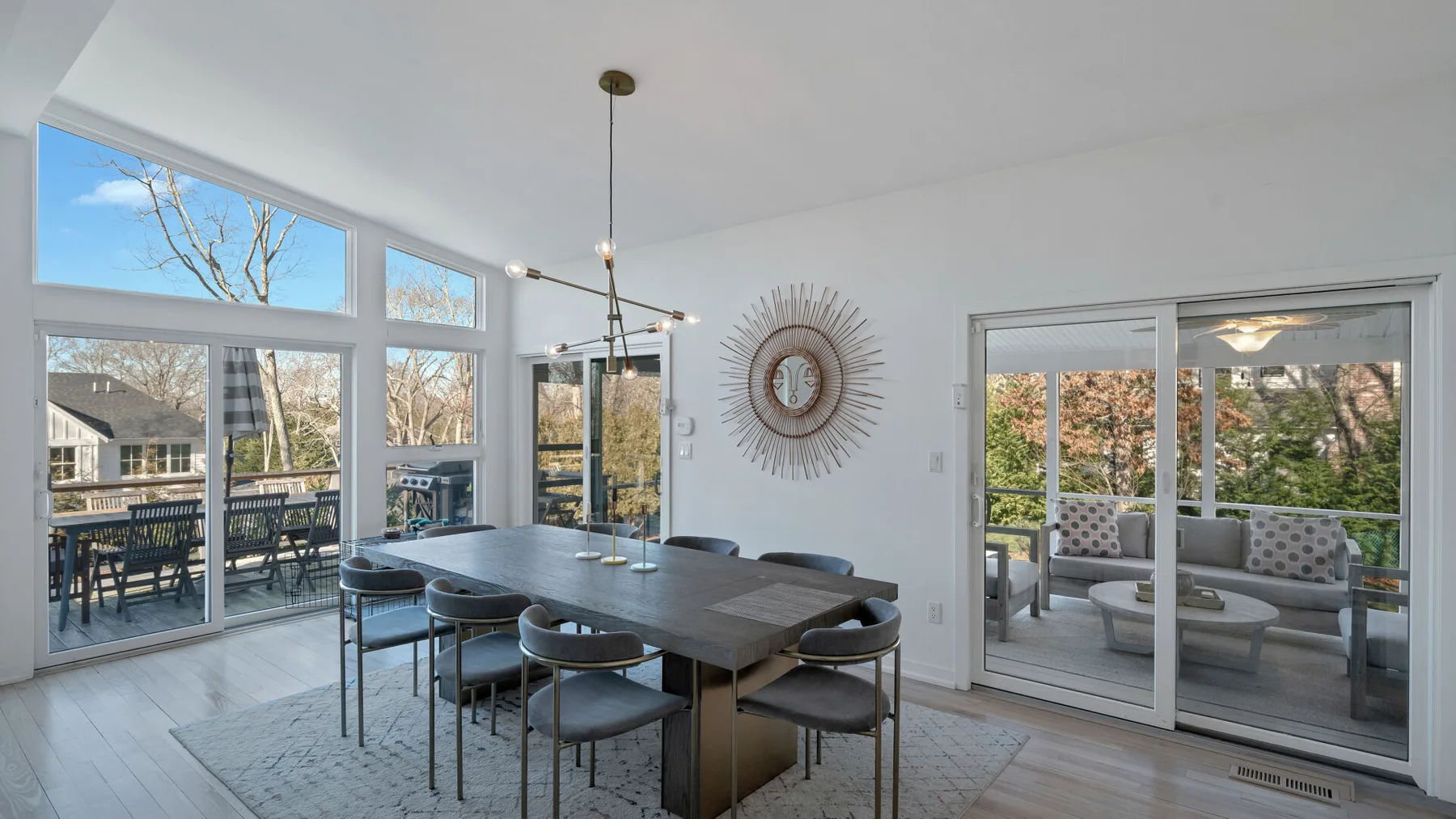 A dining area with a long table beside large windows overlooking a patio.