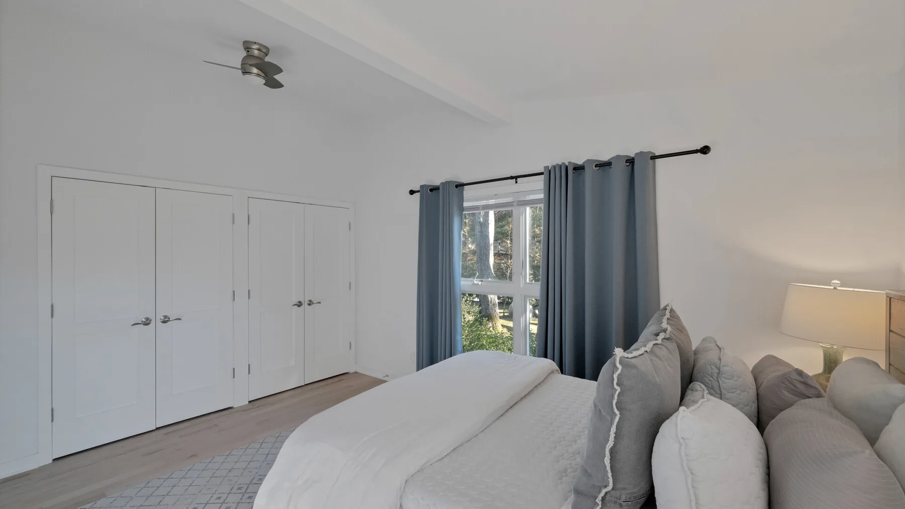A bedroom with a bed, blue curtains, and a row of white closet doors.