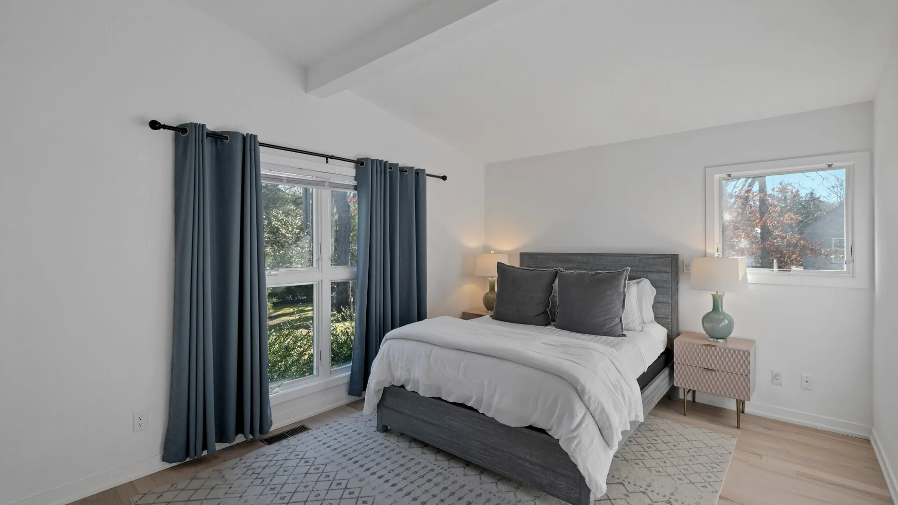 A bedroom with a bed, dark curtains, and windows on two walls.