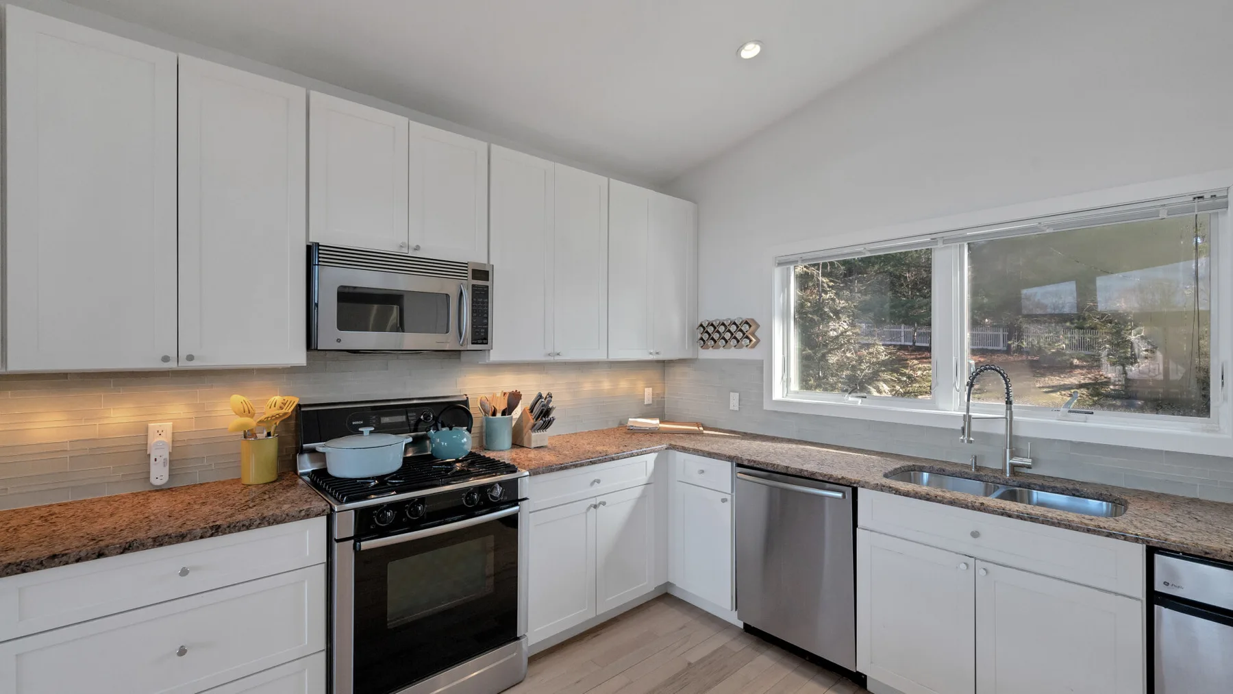 A bright kitchen with white cabinets, dark countertops, and a window above the sink.