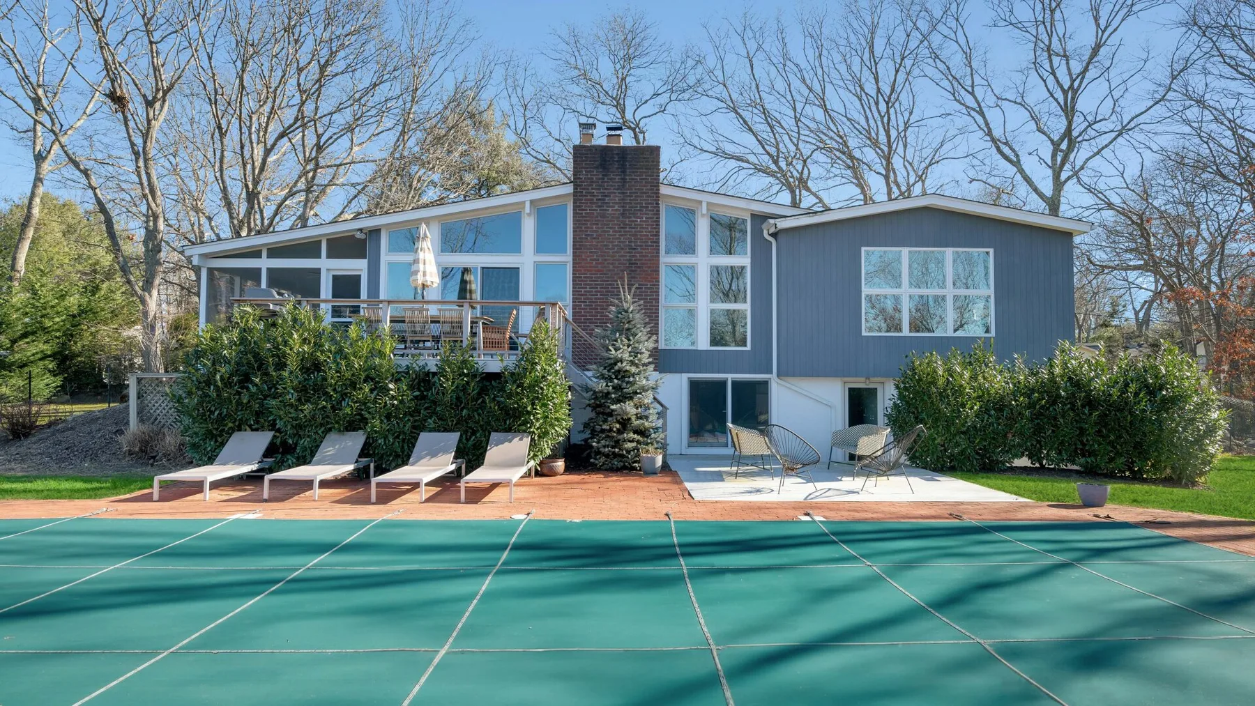 A modern house overlooks a tennis court, with a patio and outdoor seating.
