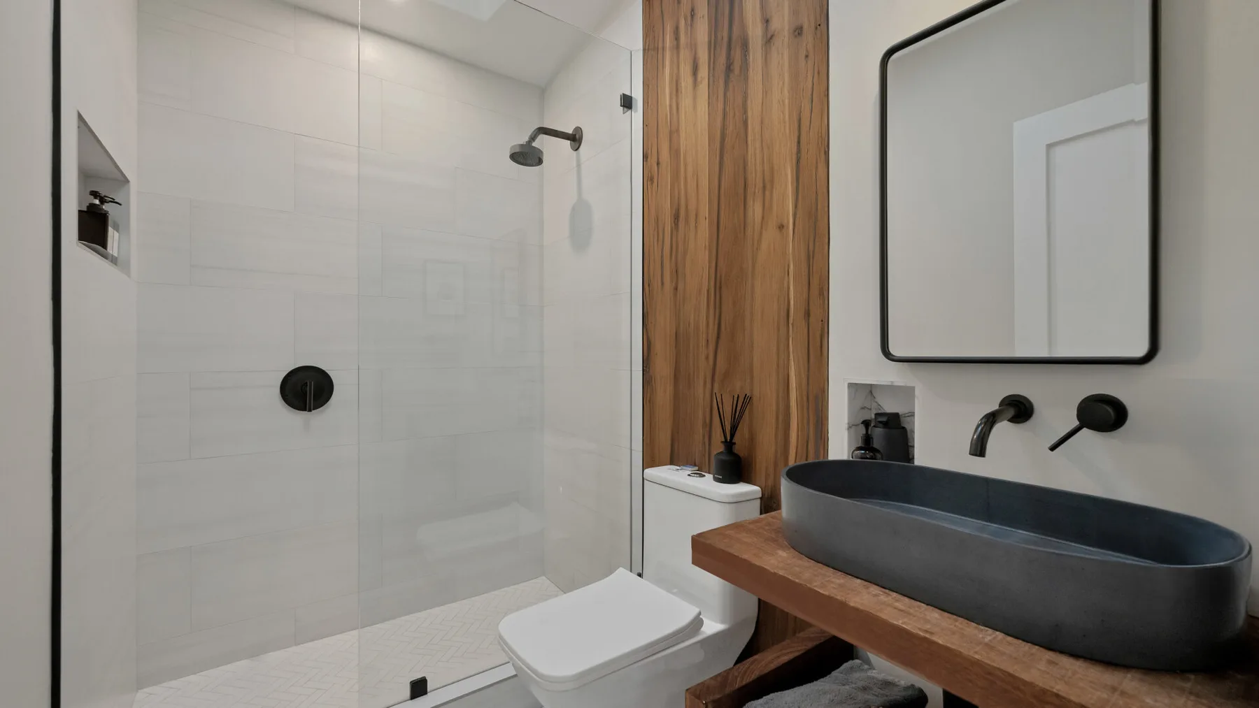A modern bathroom with a walk-in shower and a dark vessel sink.